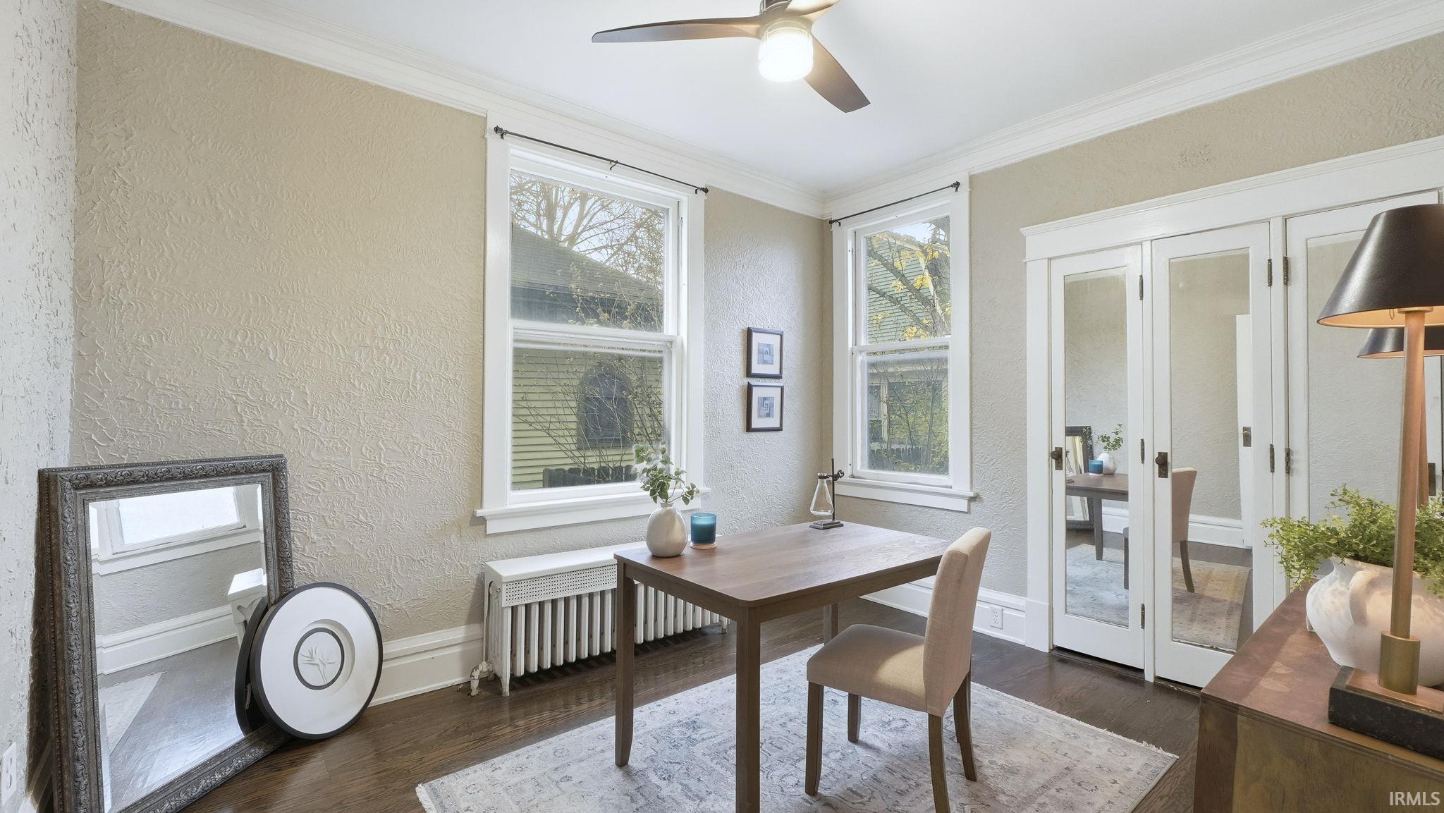 Office space with a textured wall, dark wood-style flooring, radiator, french doors, and ceiling fan