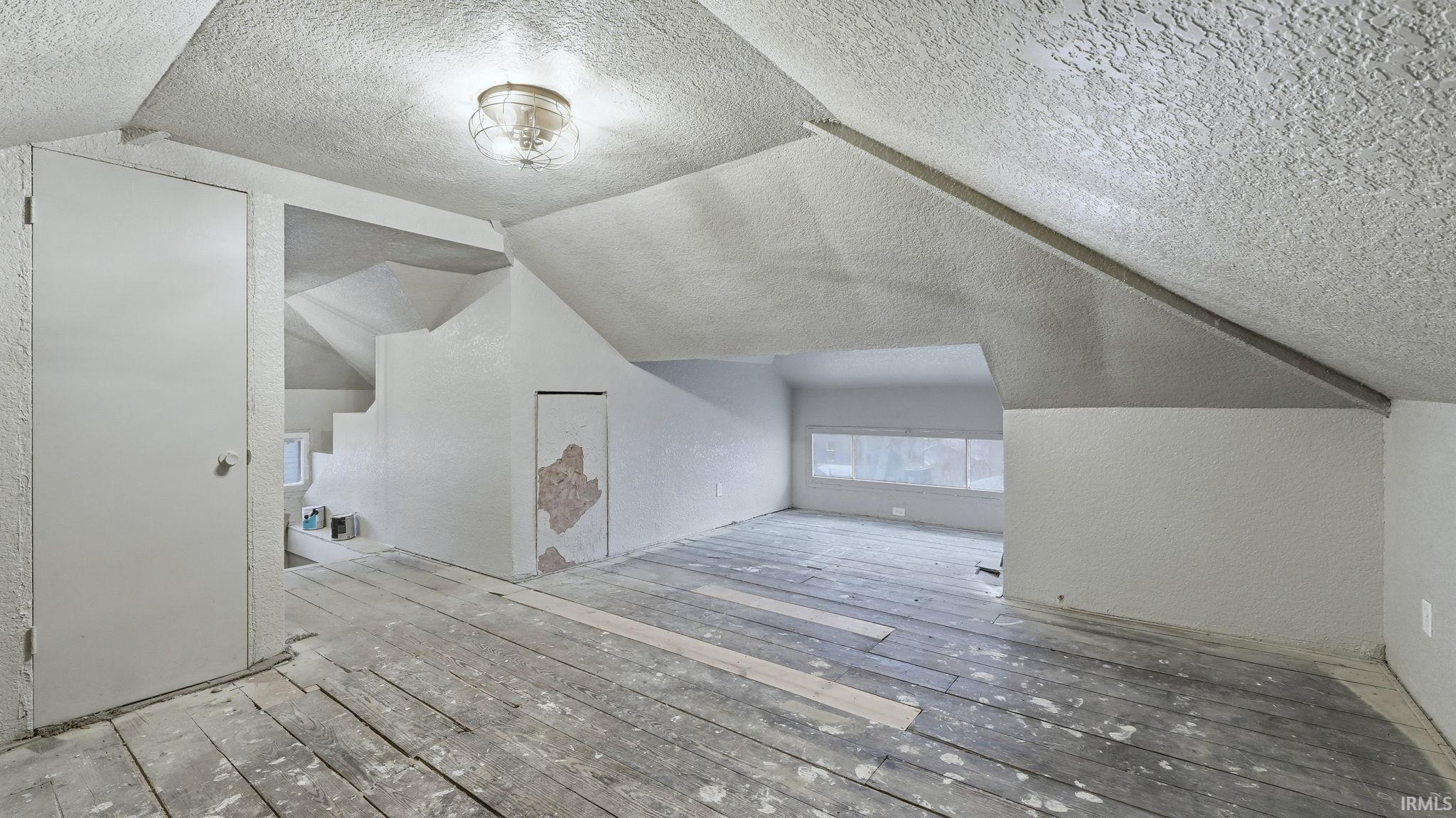 Bonus room with a textured ceiling, lofted ceiling, a textured wall, and hardwood / wood-style floors