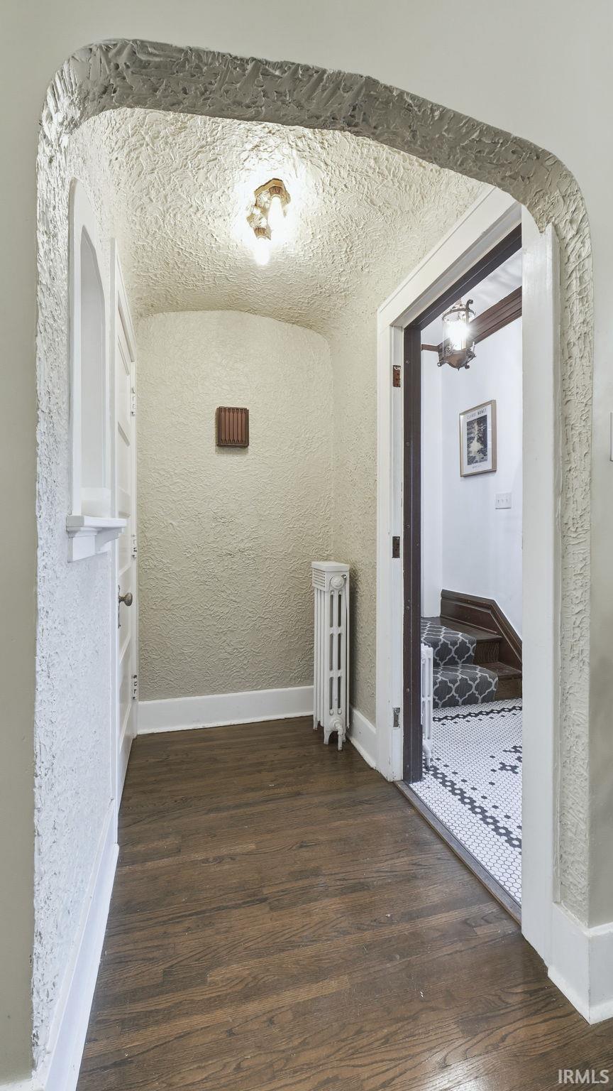Hall with a textured wall, dark wood finished floors, and radiator heating unit