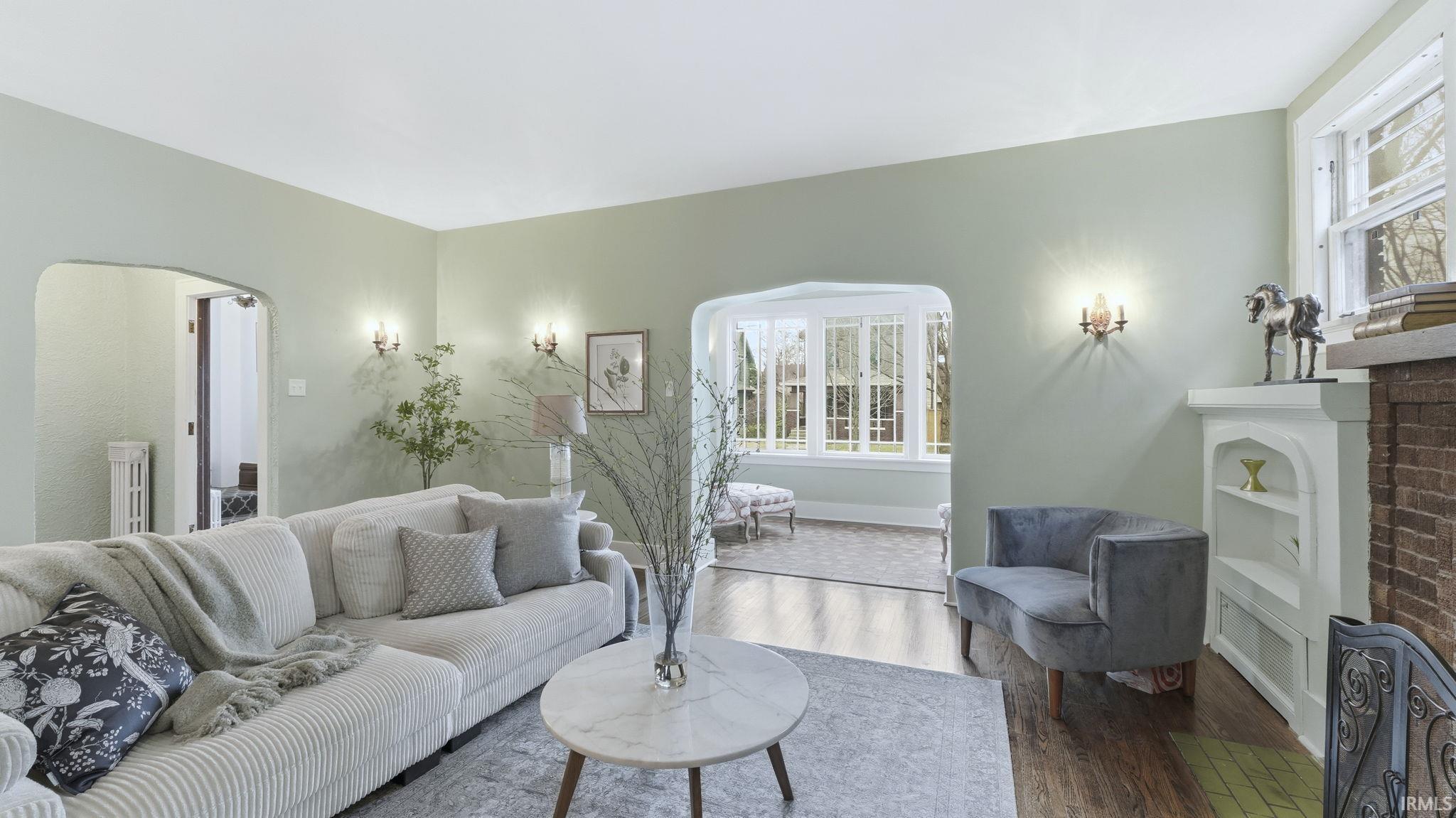 Living room featuring arched walkways, healthy amount of natural light, a brick fireplace, and wood finished floors