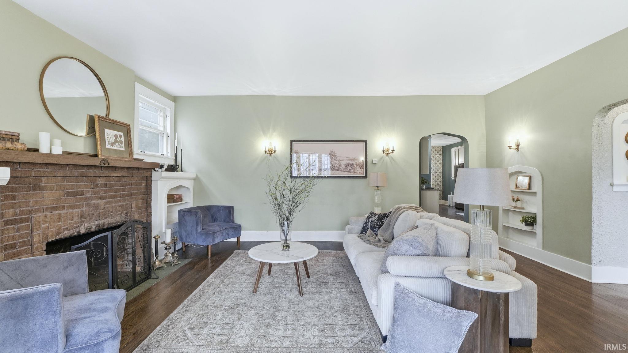 Living area with arched walkways, a brick fireplace, wood finished floors, and built in shelves