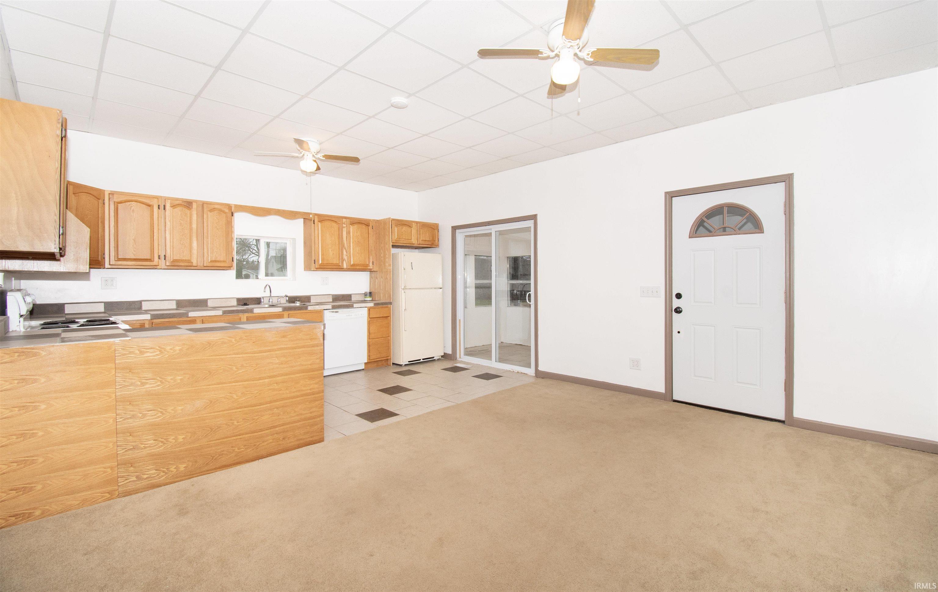Kitchen featuring ceiling fan, light colored carpet, white appliances, a drop ceiling, and light tile patterned floors