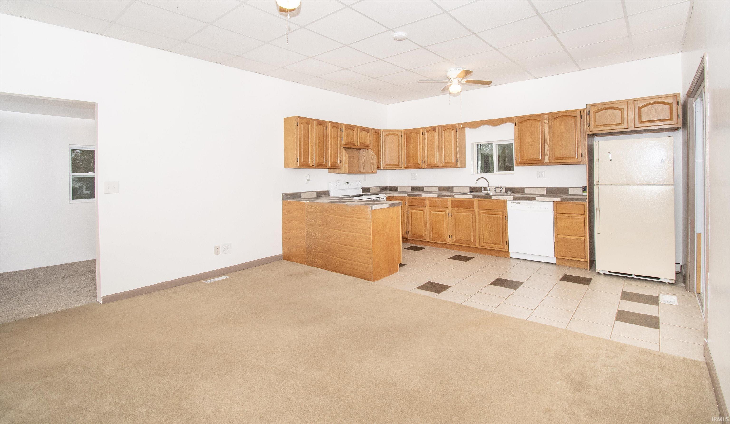 Kitchen featuring white appliances, light carpet, a drop ceiling, a ceiling fan, and light tile patterned flooring