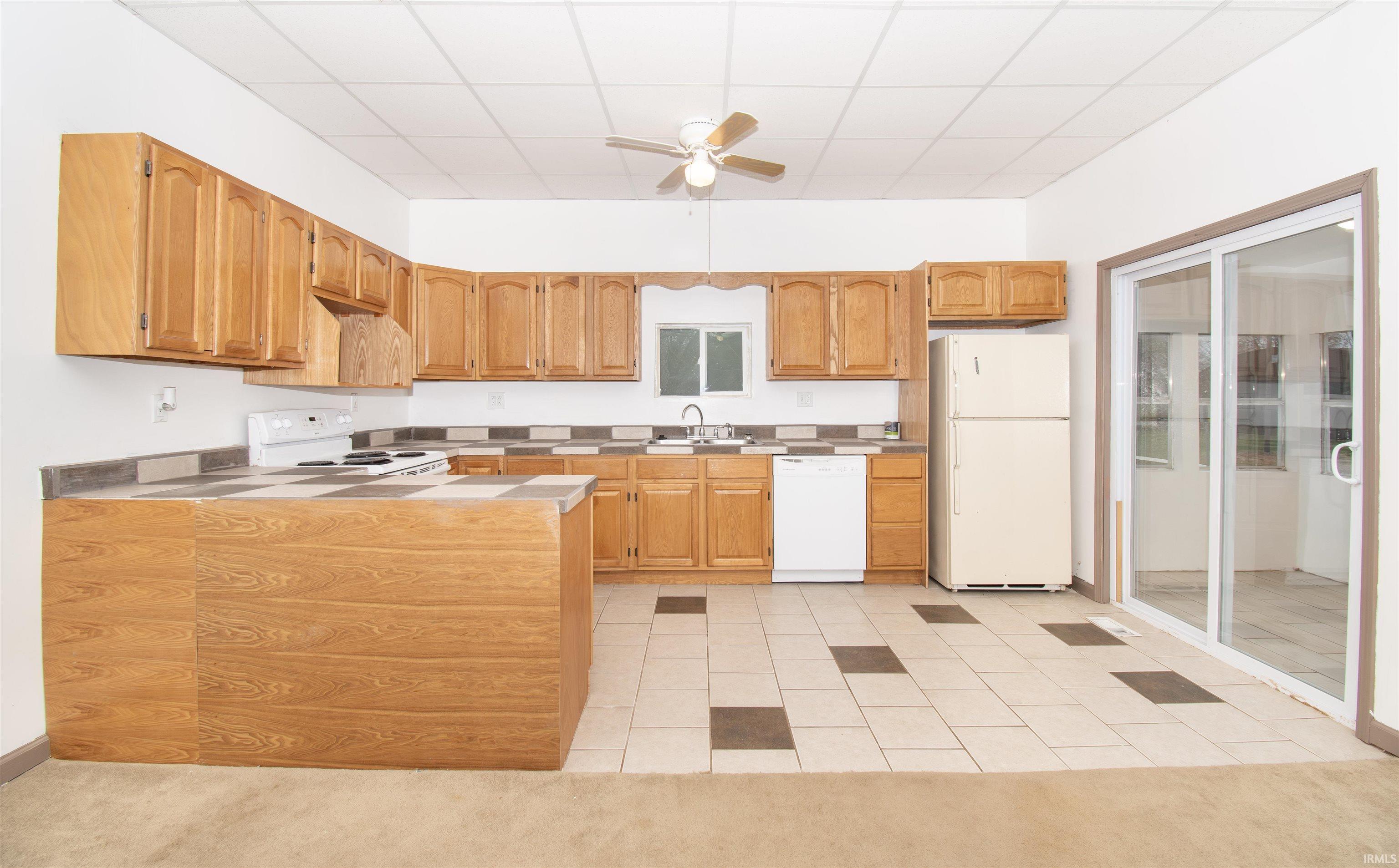 Kitchen with white appliances, a ceiling fan, light tile patterned floors, light carpet, and light countertops
