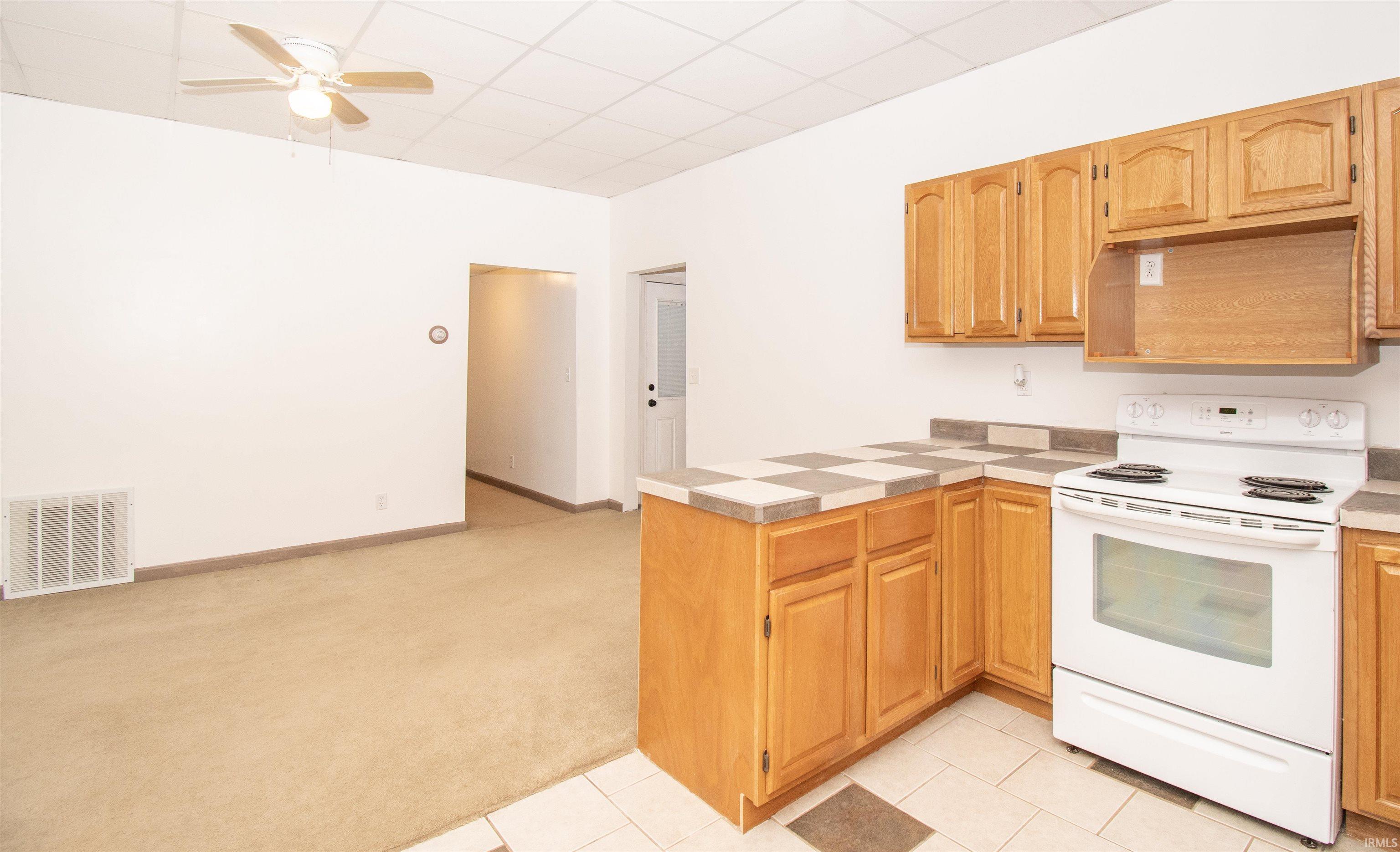 Kitchen with electric range, light colored carpet, a peninsula, ceiling fan, and light tile patterned floors