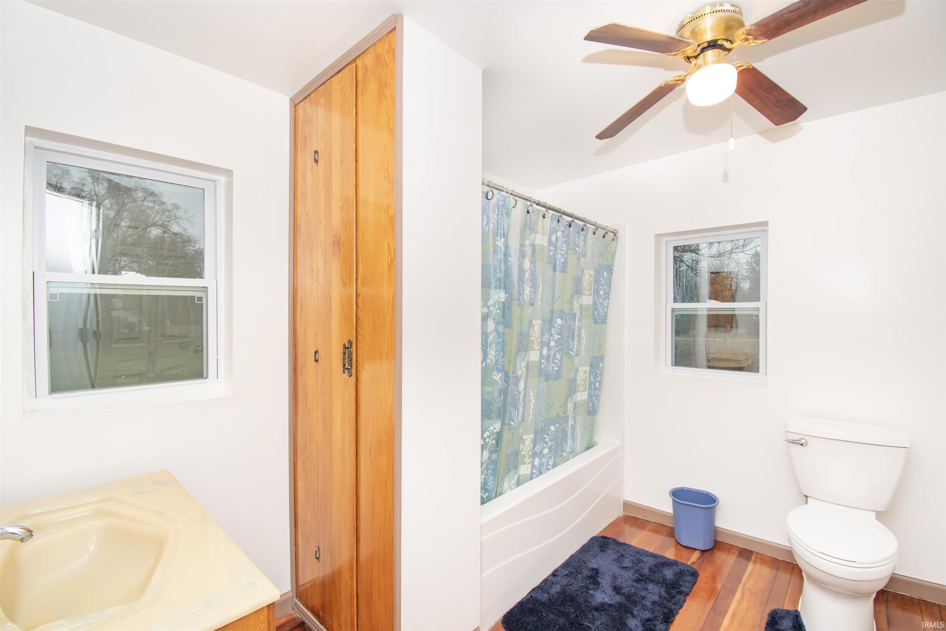 Bathroom with shower / tub combo with curtain, wood finished floors, vanity, and ceiling fan