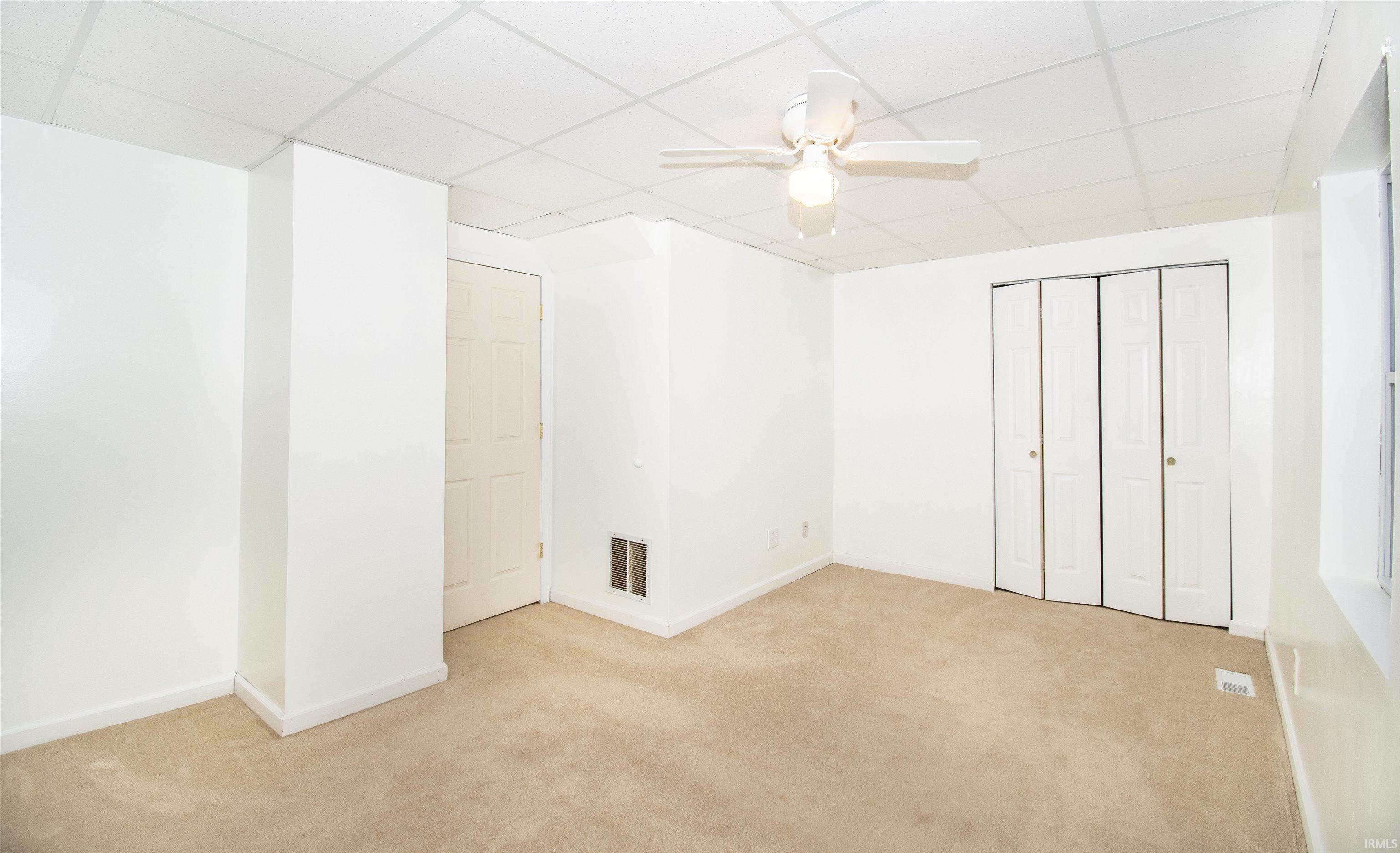 Unfurnished bedroom with light carpet, a drop ceiling, a ceiling fan, and a closet