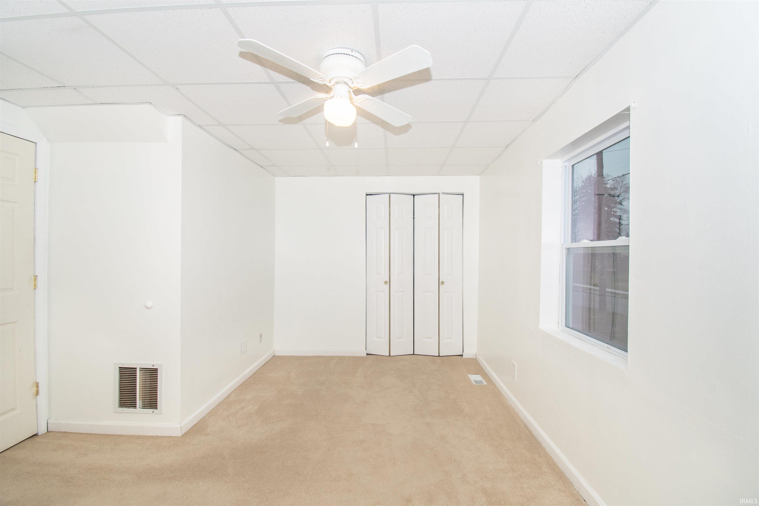 Unfurnished bedroom with a paneled ceiling, carpet floors, a ceiling fan, and a closet