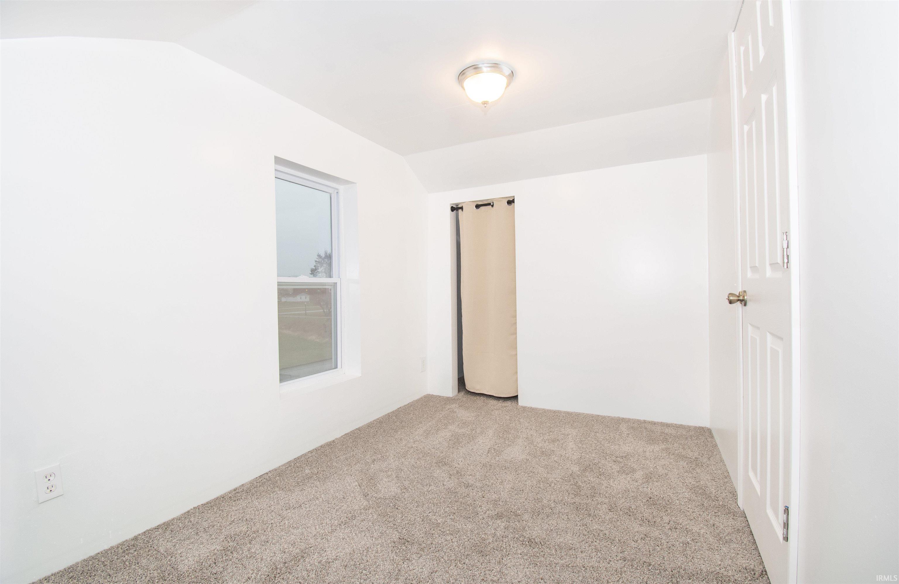Carpeted spare room with vaulted ceiling