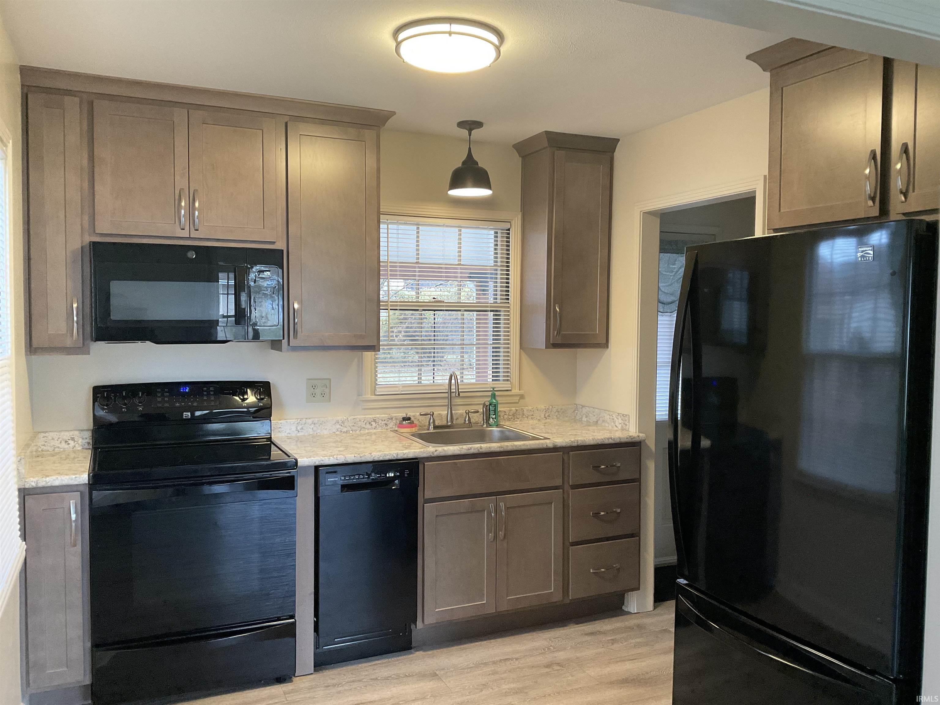 Kitchen featuring black appliances, light countertops, light wood finished floors, and hanging light fixtures
