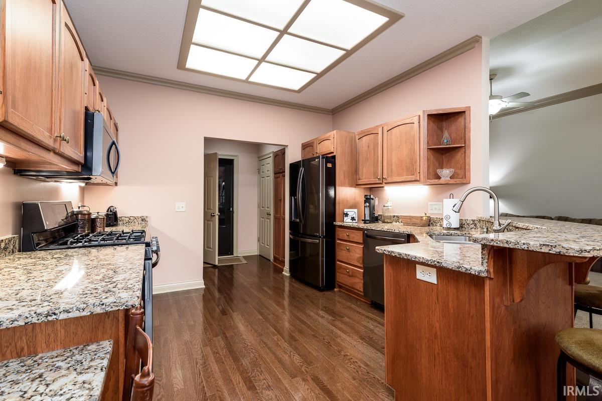 Kitchen featuring ornamental molding, light stone countertops, stainless steel appliances, dark wood-style floors, and a peninsula