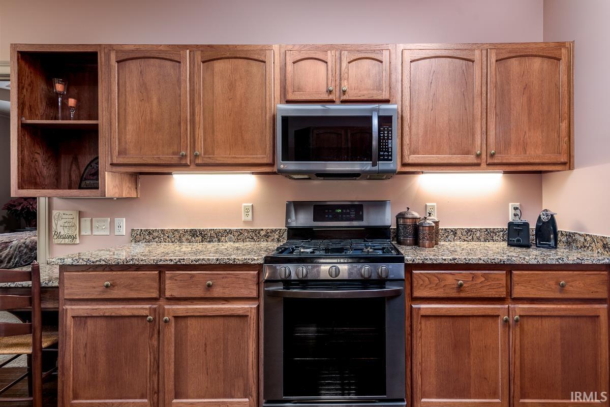 Kitchen featuring appliances with stainless steel finishes, open shelves, light stone countertops, and brown cabinets