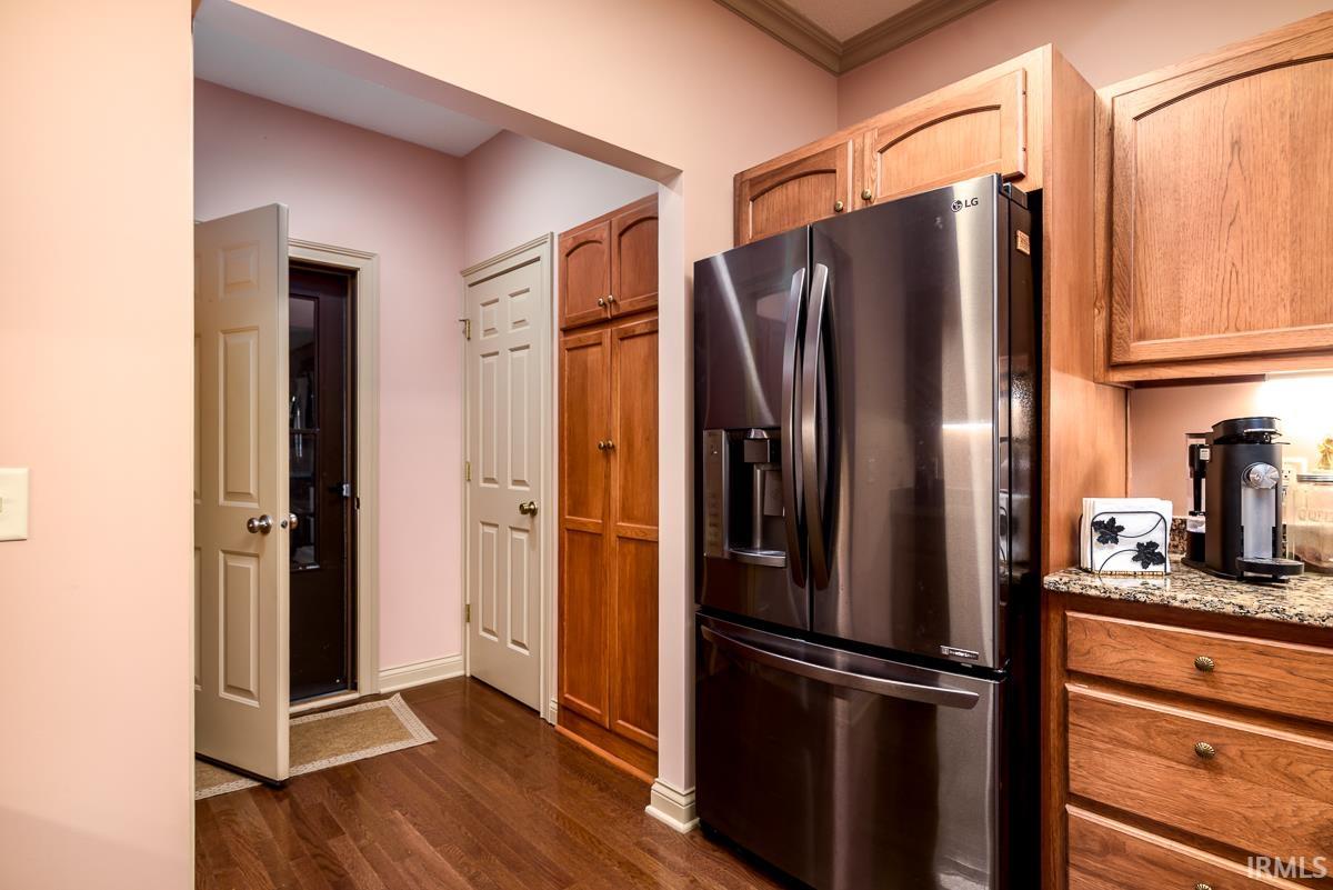 Kitchen featuring stainless steel fridge with ice dispenser, dark wood-style flooring, light stone counters, brown cabinetry, and ornamental molding