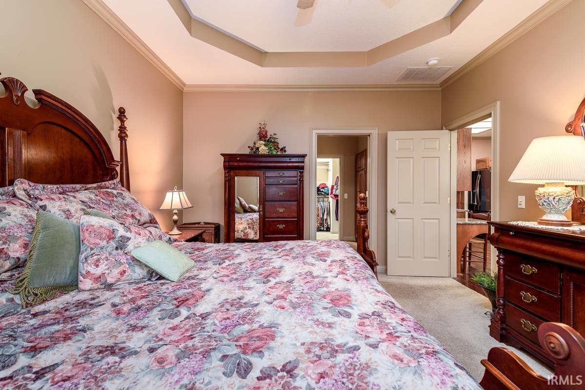 Bedroom with a tray ceiling, light carpet, ceiling fan, crown molding, and fridge with ice dispenser