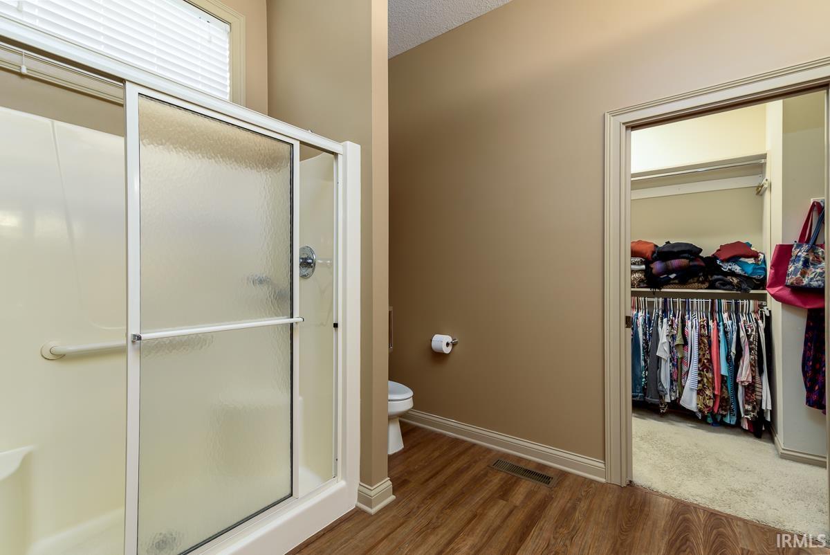 Bathroom featuring a stall shower, a spacious closet, a textured ceiling, and wood finished floors