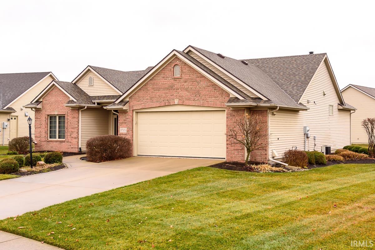 View of front of house with brick siding, a front yard, roof with shingles, driveway, and a garage