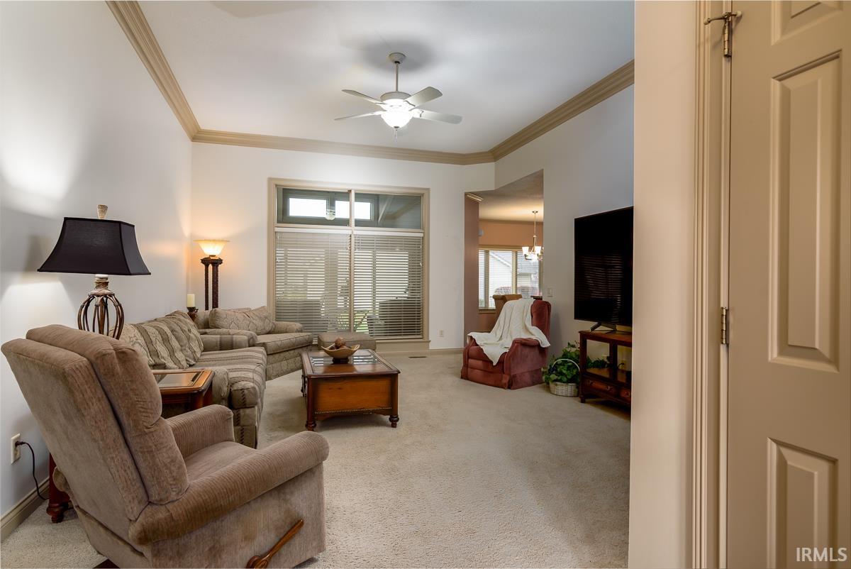 Living room with ornamental molding, ceiling fan, light carpet, and a chandelier