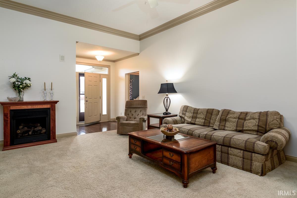 Carpeted living area with ornamental molding, a fireplace, and a ceiling fan