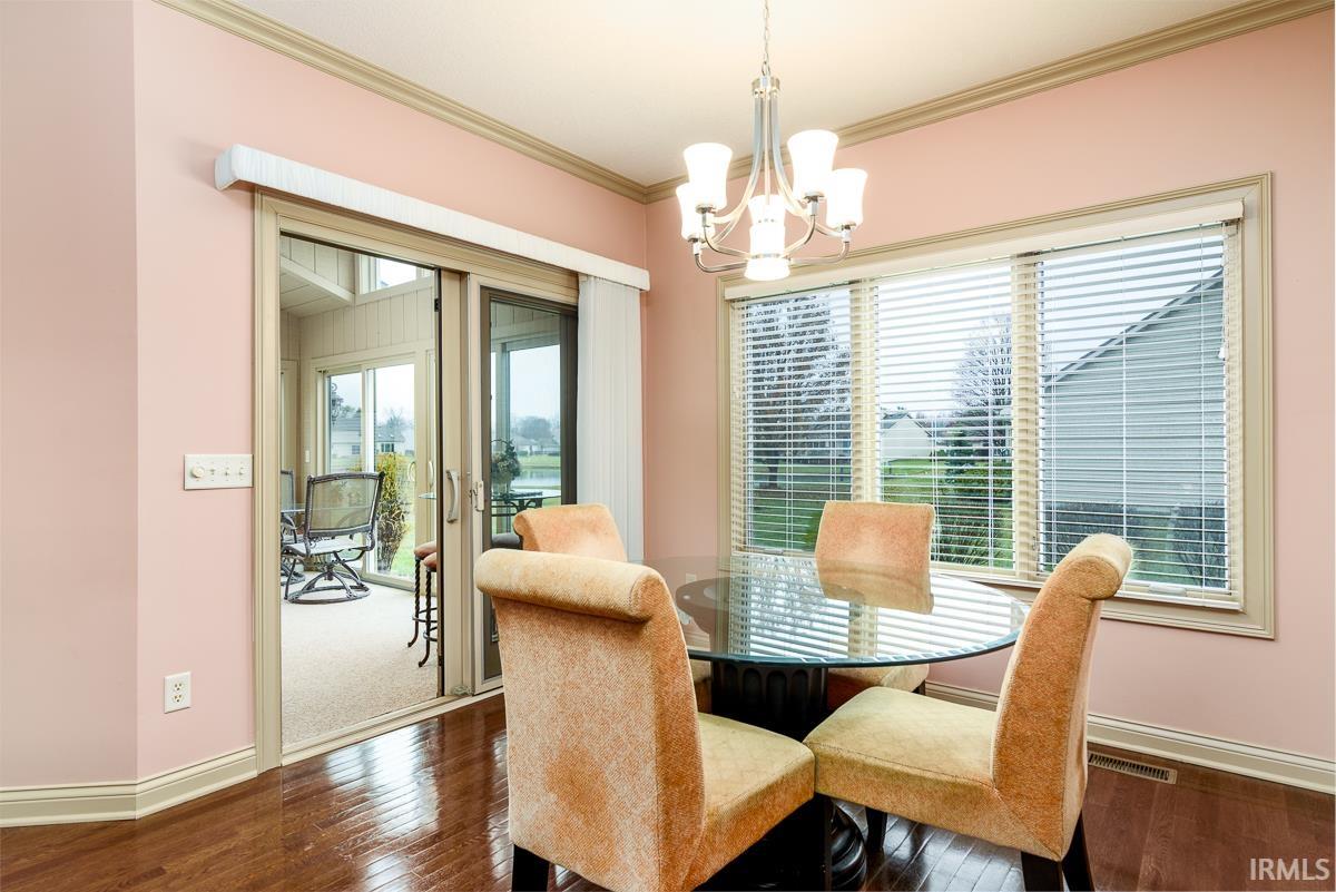 Dining area with dark wood-type flooring, ornamental molding, and a chandelier