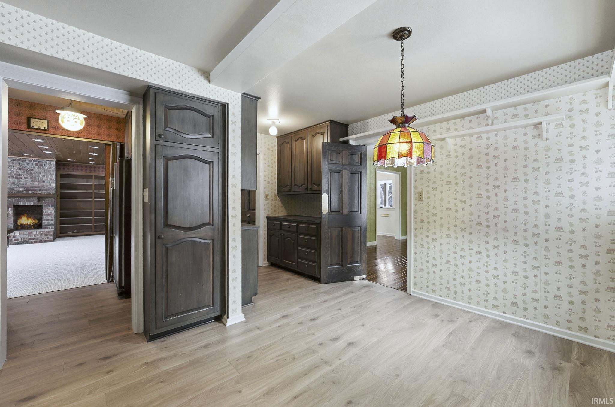 Unfurnished dining area with wallpapered walls, light wood-style floors, and a brick fireplace
