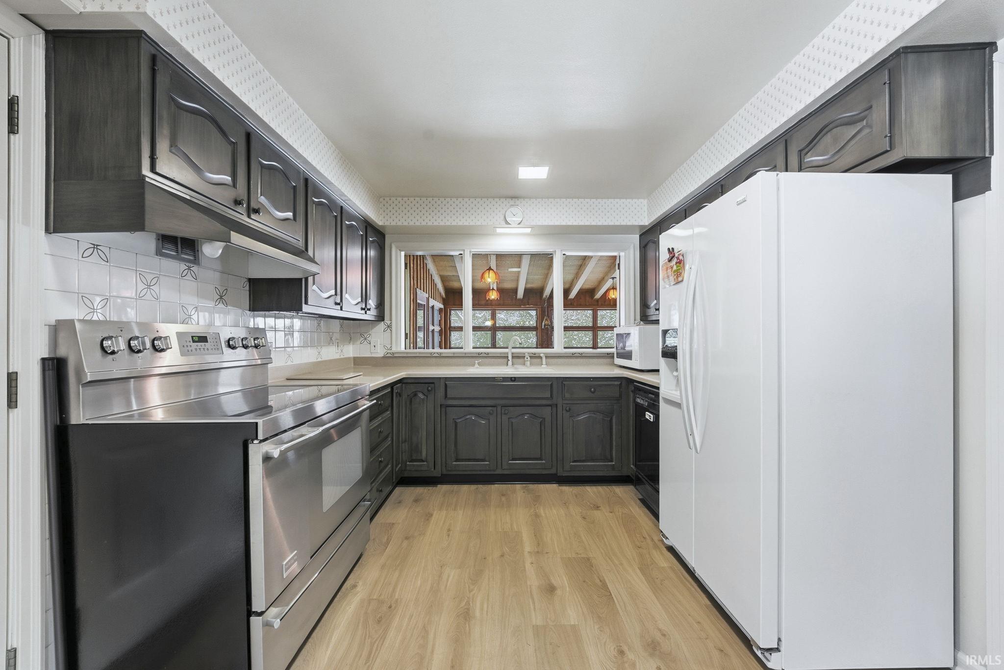 Kitchen with white appliances, light wood-type flooring, light countertops, and backsplash