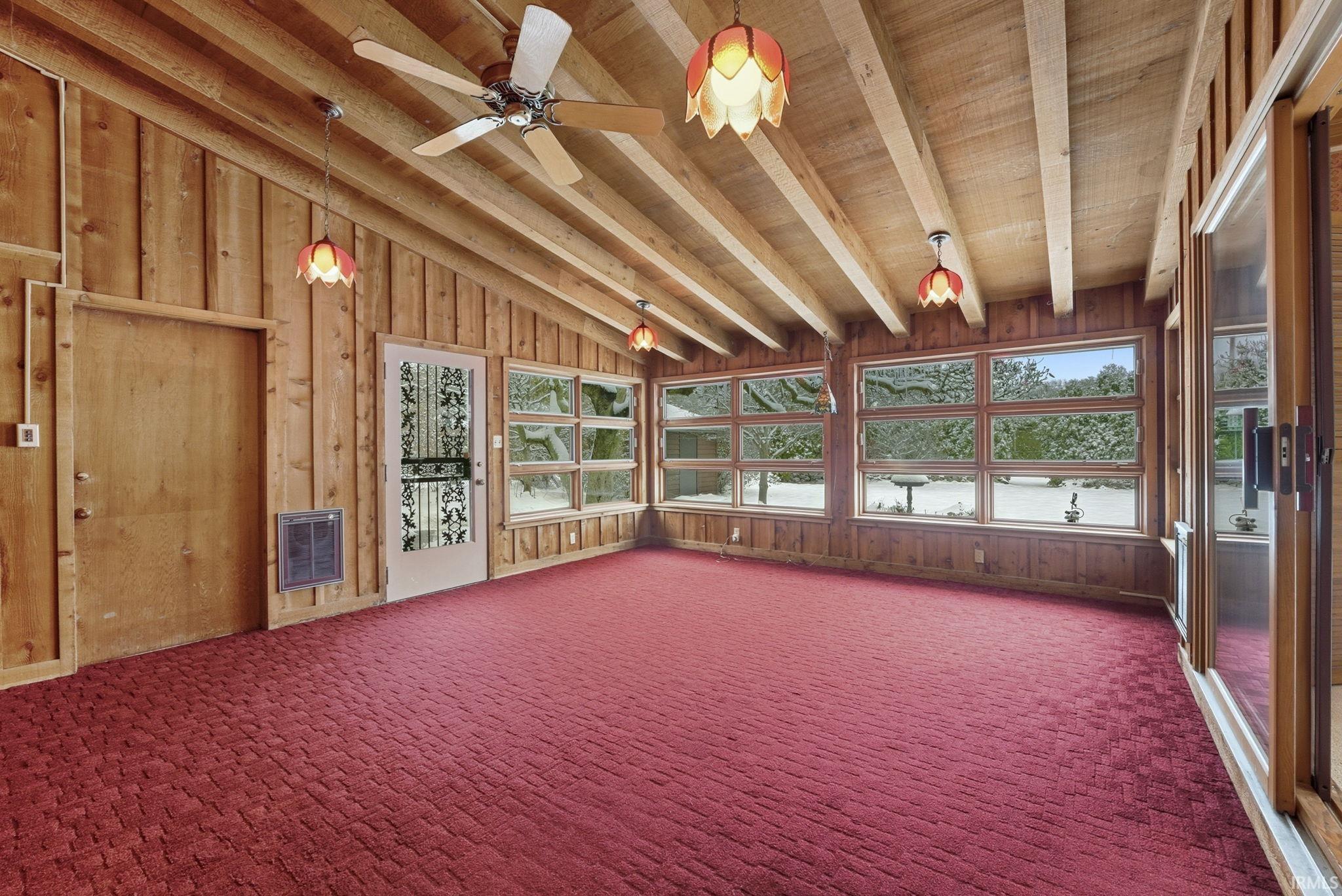Unfurnished sunroom featuring wood walls, heating unit, wood ceiling, and carpet
