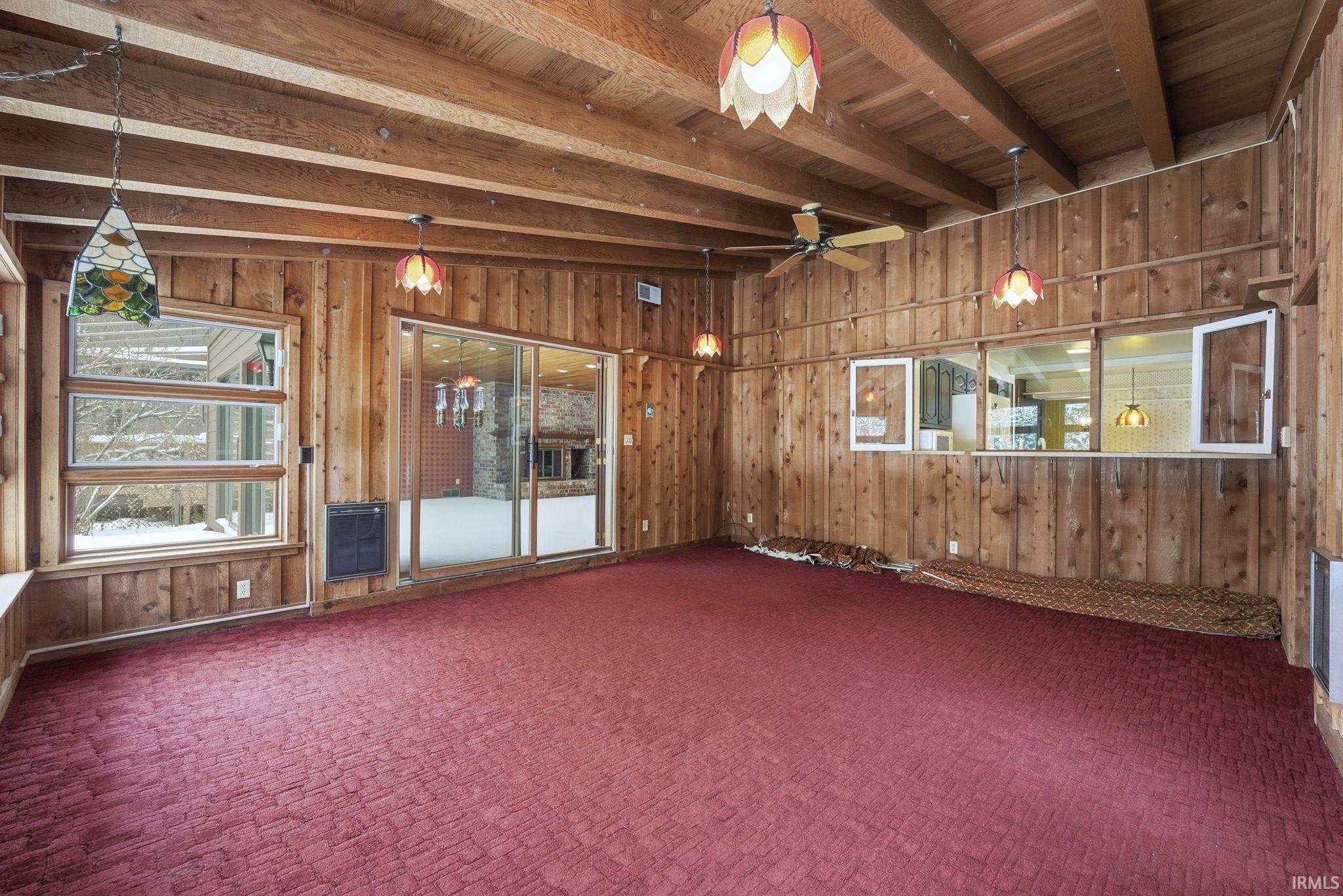 Spare room featuring wooden walls, heating unit, carpet, a wooden ceiling with exposed beams, and a ceiling fan