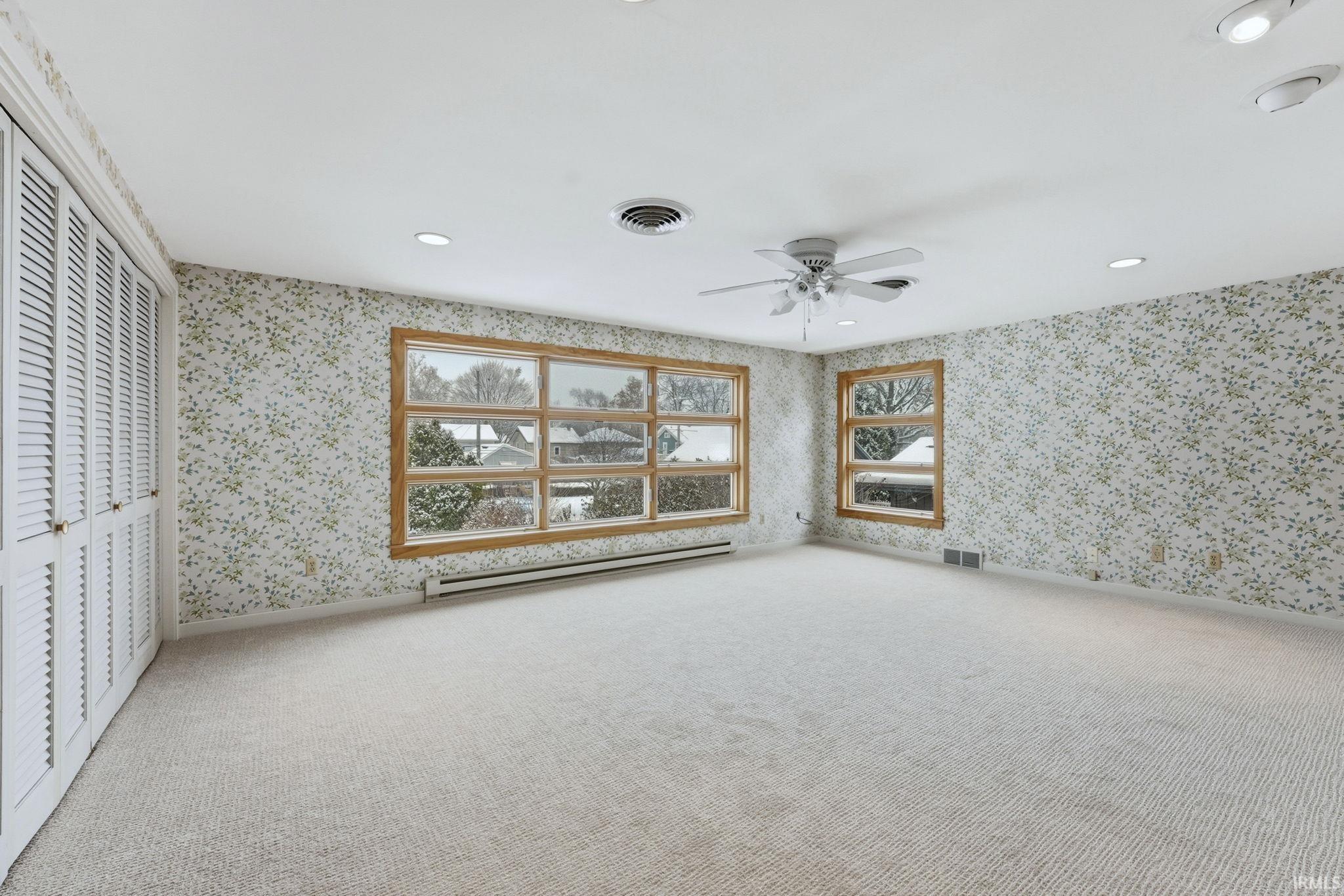 Unfurnished bedroom featuring a baseboard heating unit, wallpapered walls, a ceiling fan, carpet flooring, and a closet