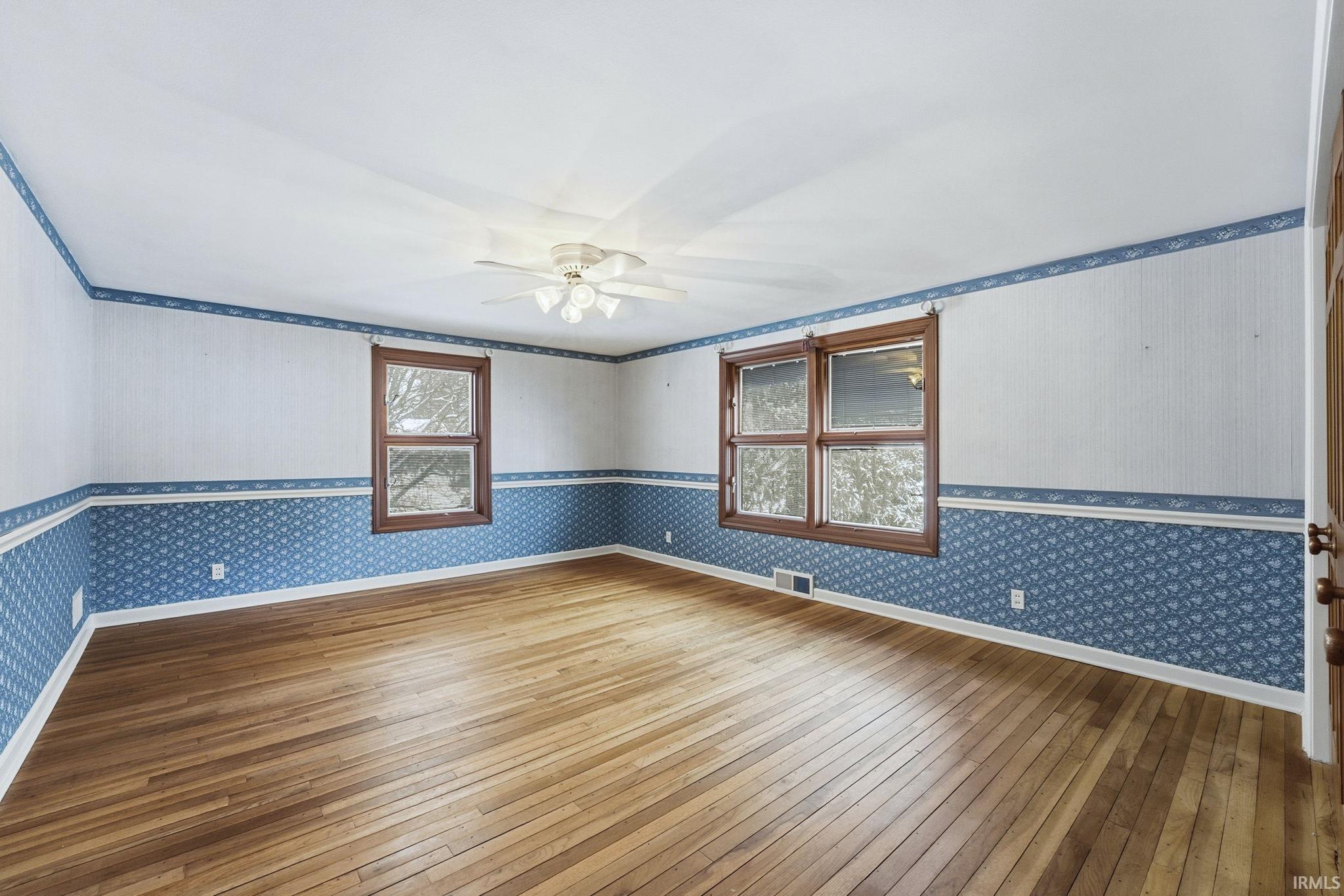 Spare room with wallpapered walls, hardwood / wood-style flooring, and a ceiling fan