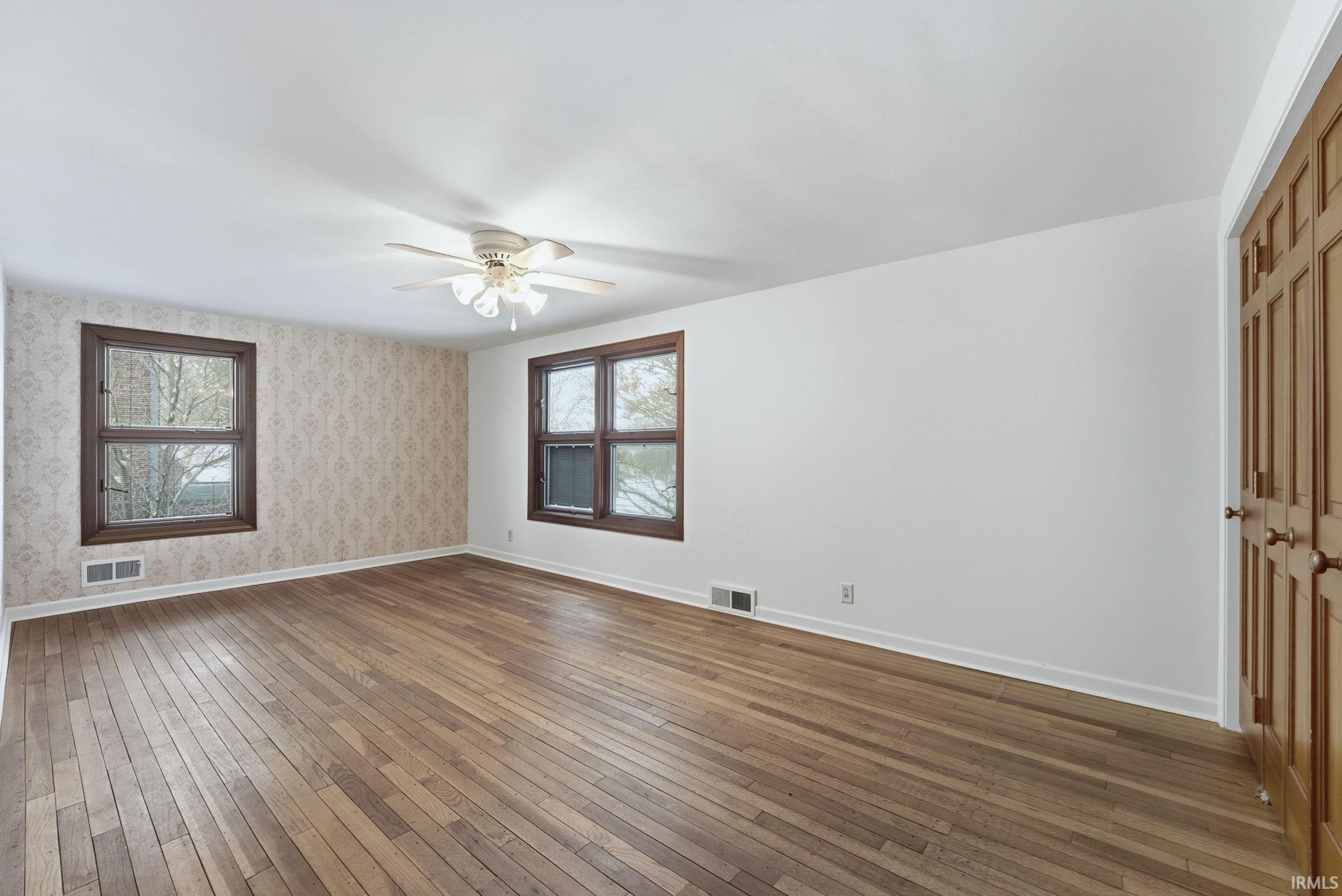 Spare room featuring wood-type flooring, ceiling fan, and wallpapered walls