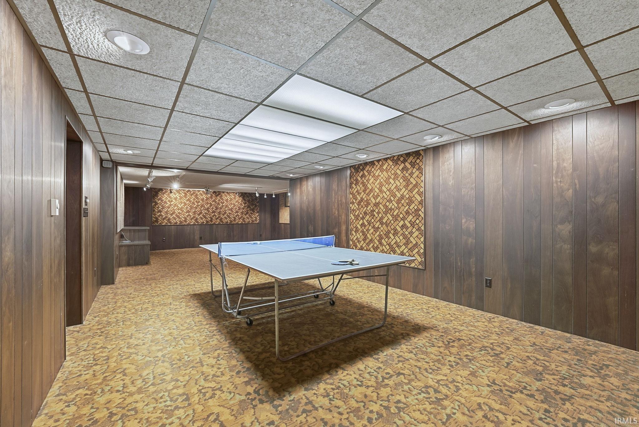 Playroom featuring wooden walls, a drop ceiling, and recessed lighting