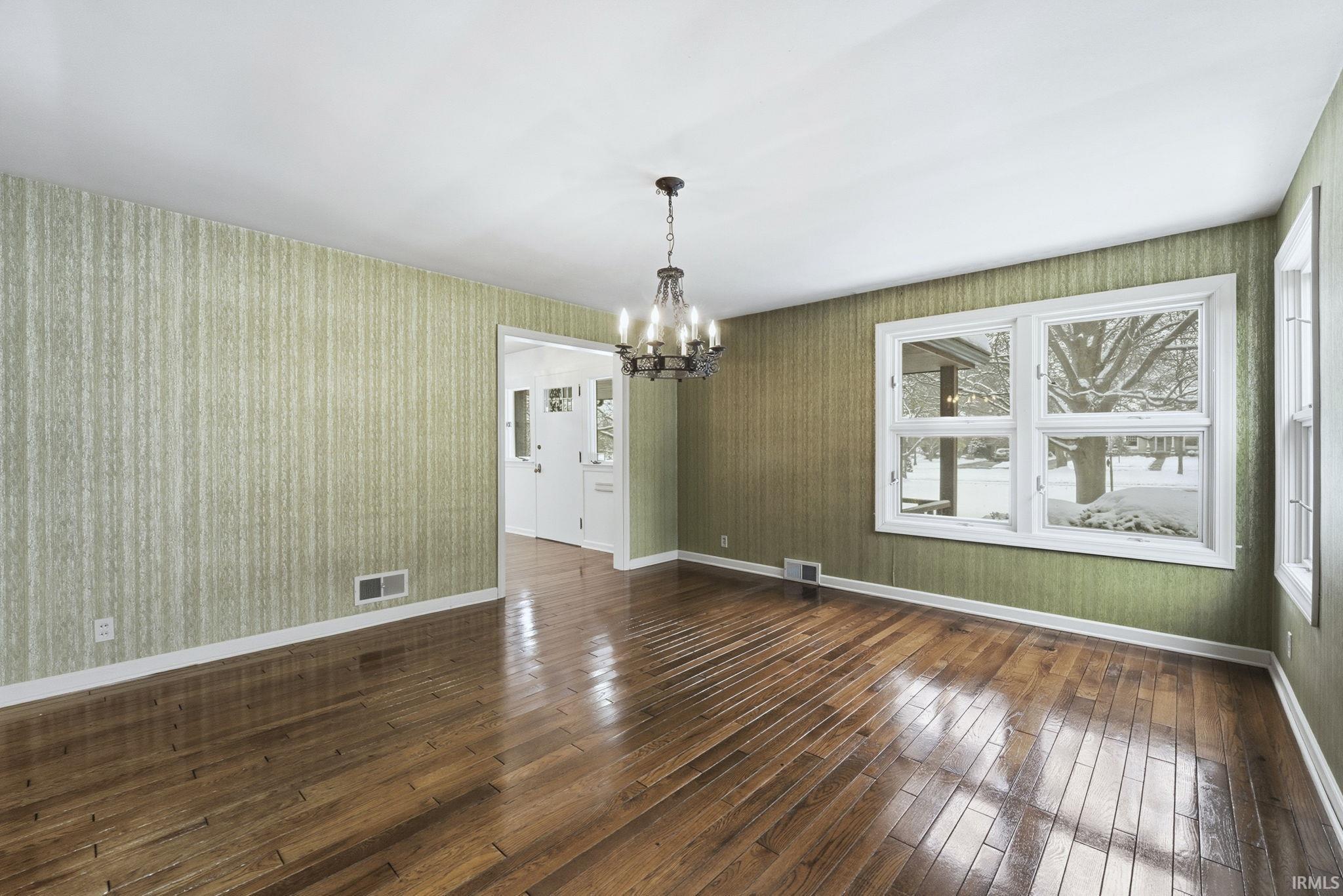 Unfurnished dining area featuring a chandelier, wallpapered walls, and dark wood-style floors