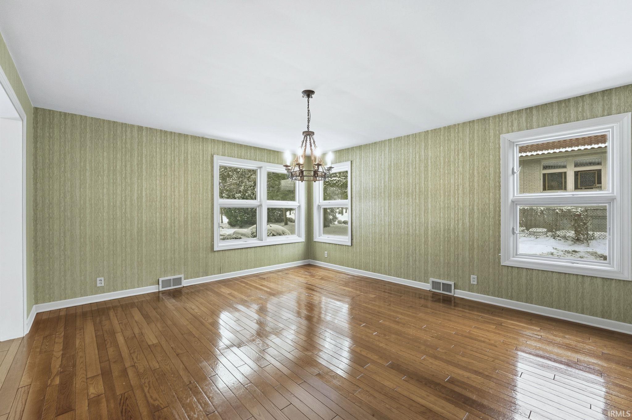 Spare room with hardwood / wood-style floors, a chandelier, and wallpapered walls
