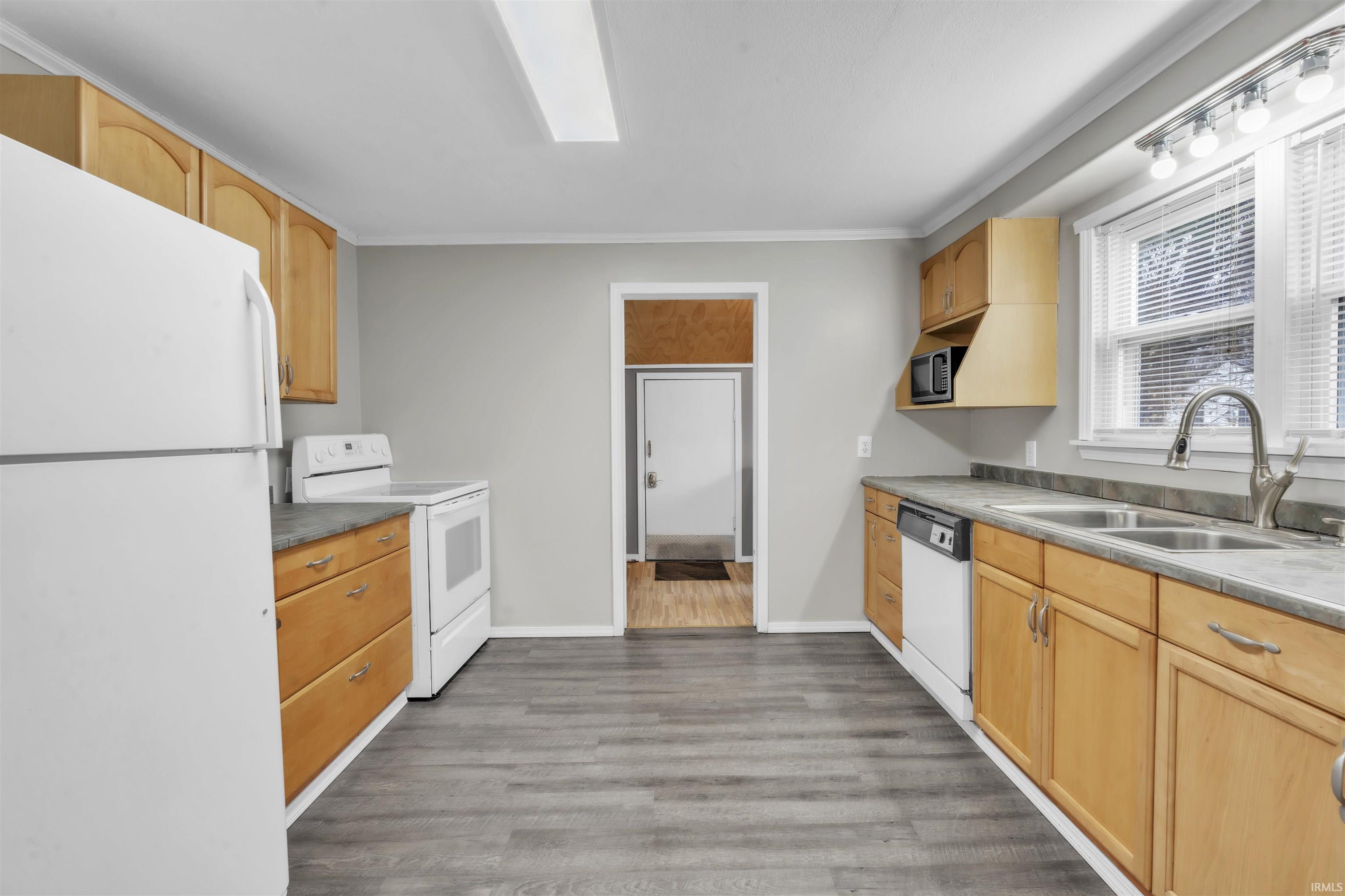 Kitchen featuring white appliances, light brown cabinets, light wood finished floors, crown molding, and light countertops