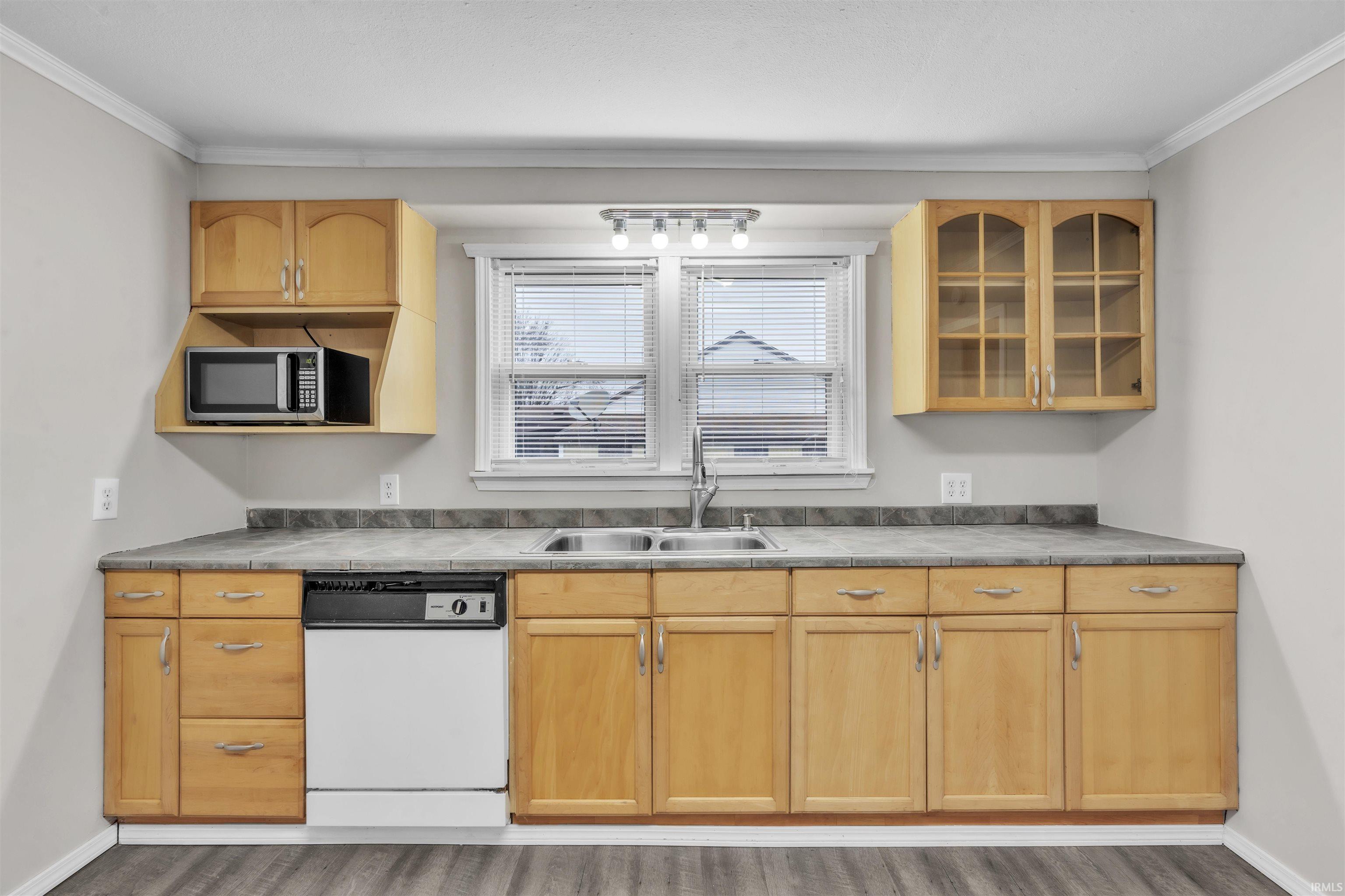 Kitchen with dishwasher, ornamental molding, stainless steel microwave, wood finished floors, and light brown cabinetry