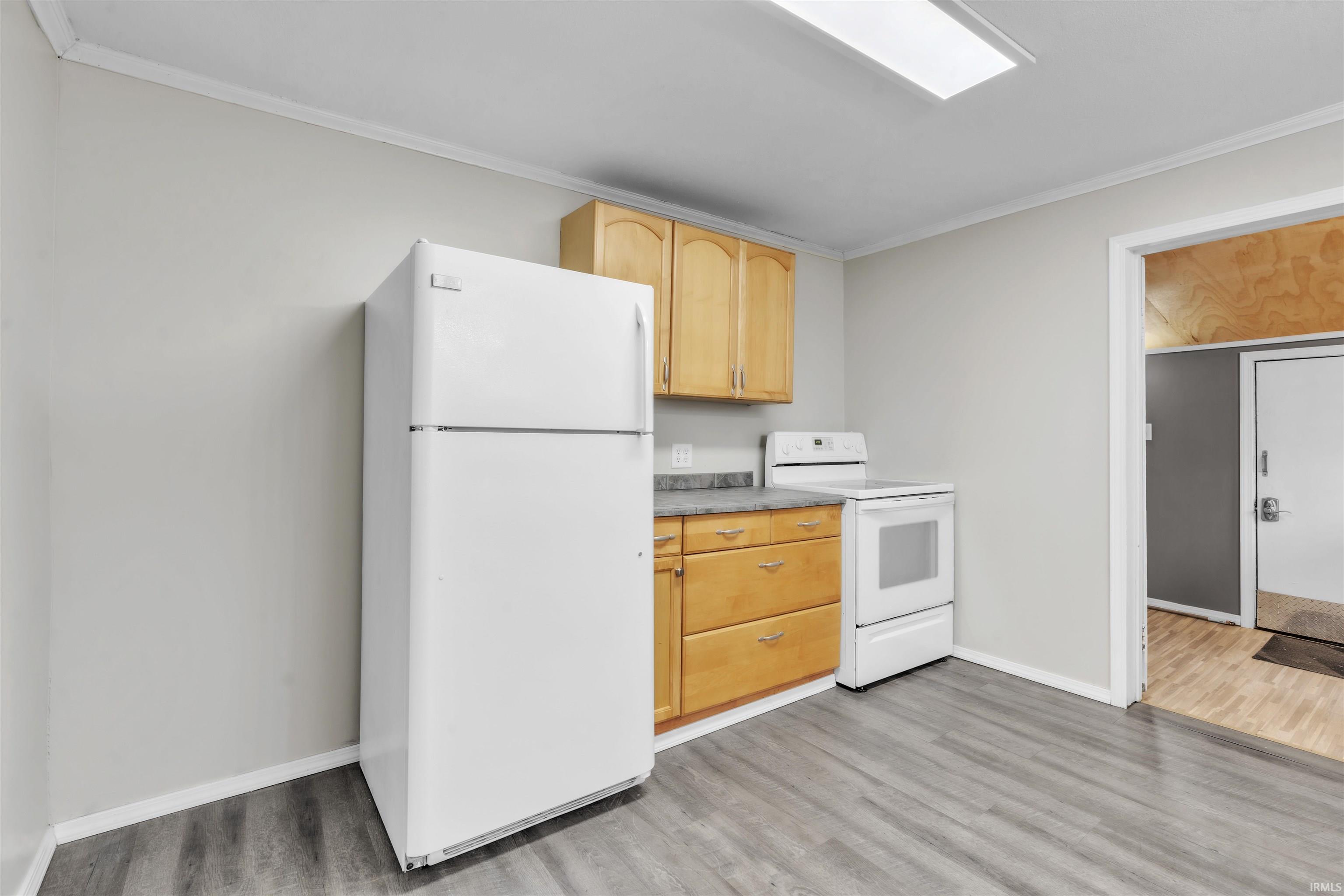 Kitchen featuring white appliances, light brown cabinetry, ornamental molding, light countertops, and light wood-style floors