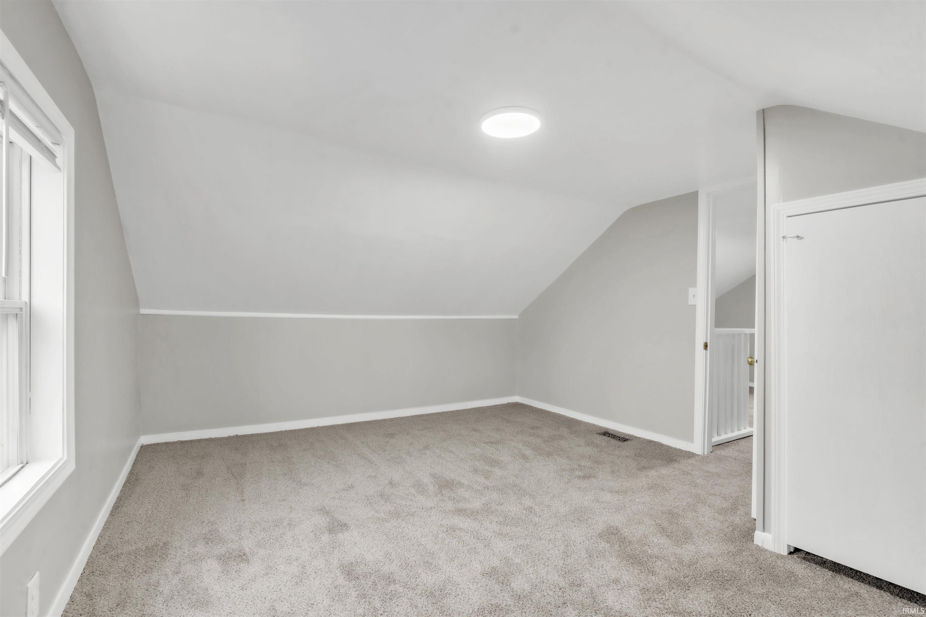 Additional living space featuring light carpet and vaulted ceiling