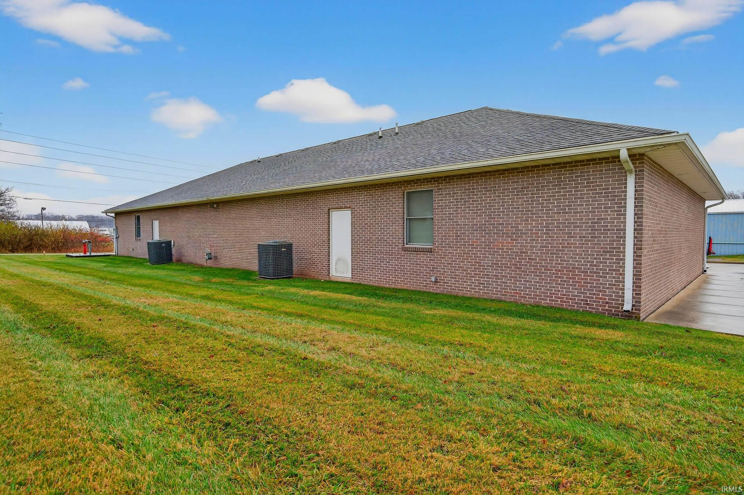View of property exterior featuring a yard, brick siding, and a shingled roof