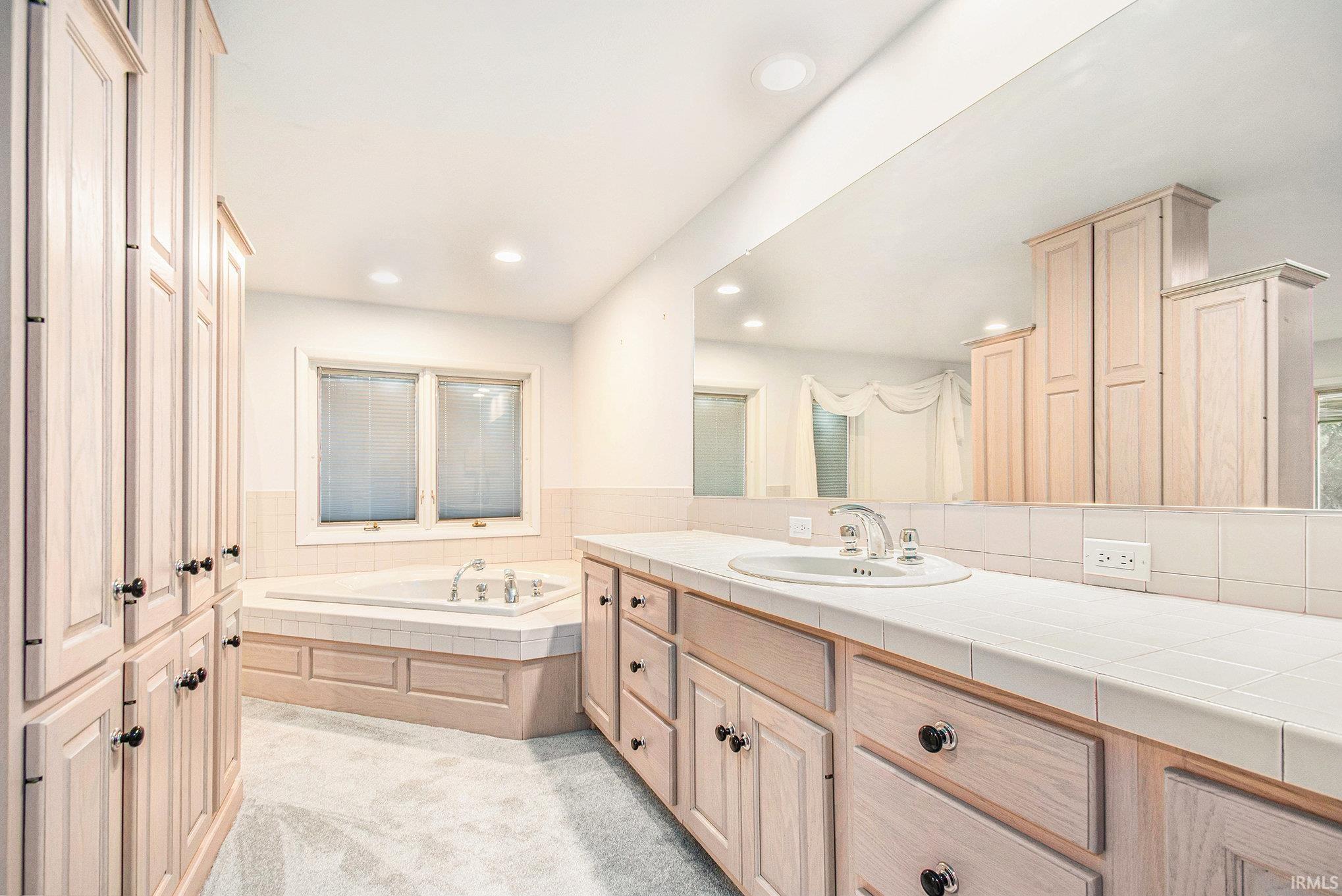 Main Bedroom Full bathroom featuring a  walk in closet, vanity, light colored carpet, a bath, and recessed lighting