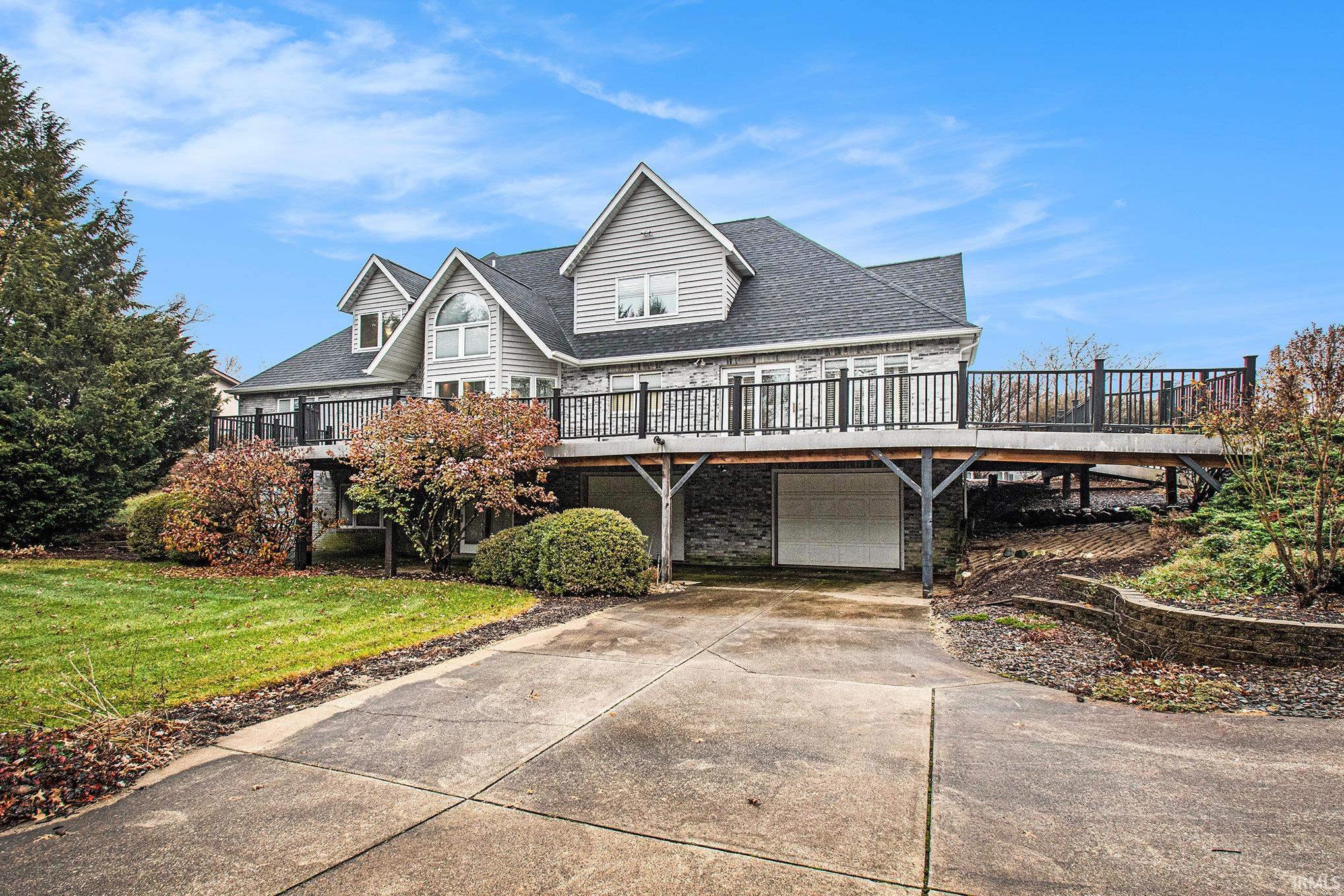 Rear View of of home showing deck, and driveway to lower level garage. Fire pit area and terrace outdoors in the back of the house