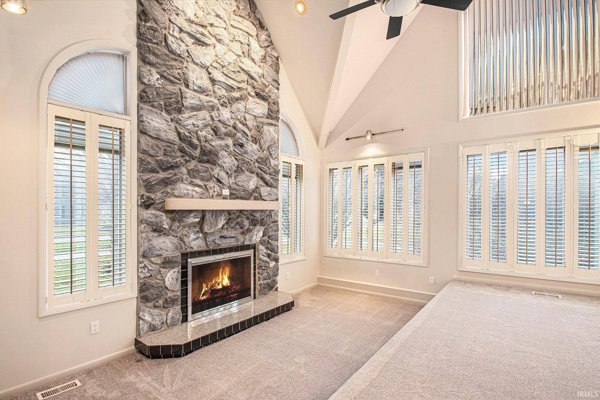 Living room featuring high vaulted ceiling, a fireplace, healthy amount of natural light, and carpet. Custom wood shutters throughout.