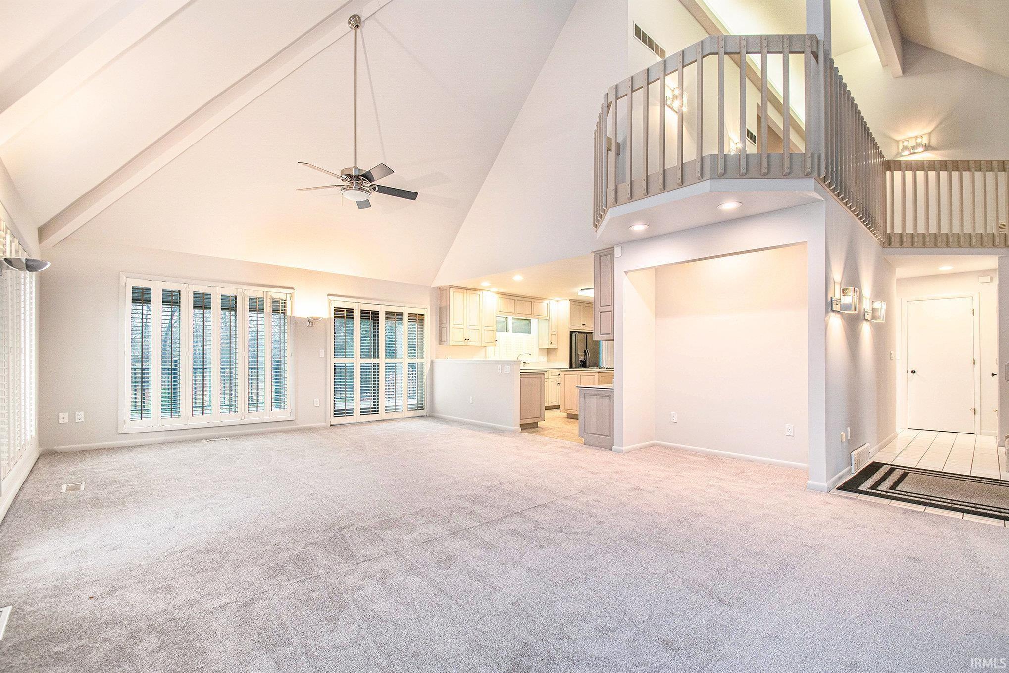 Unfurnished living room with beam ceiling, high vaulted ceiling, a ceiling fan, and light carpet
