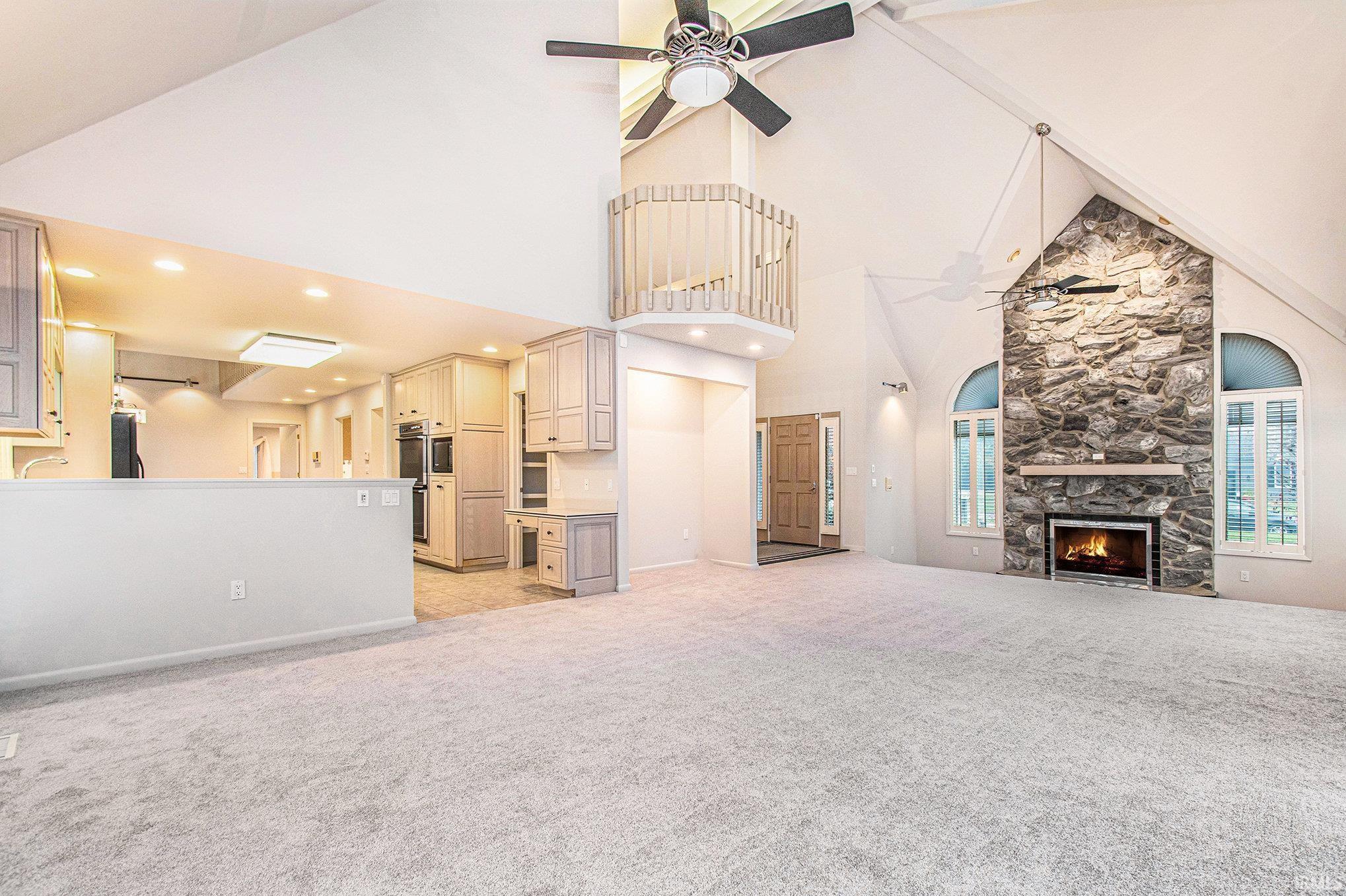 Unfurnished living room featuring a ceiling fan, a fireplace, light colored carpet, and high vaulted ceiling