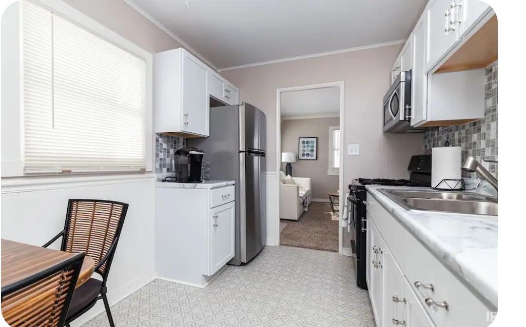 Kitchen featuring ornamental molding, black gas range, white cabinets, light countertops, and light floors