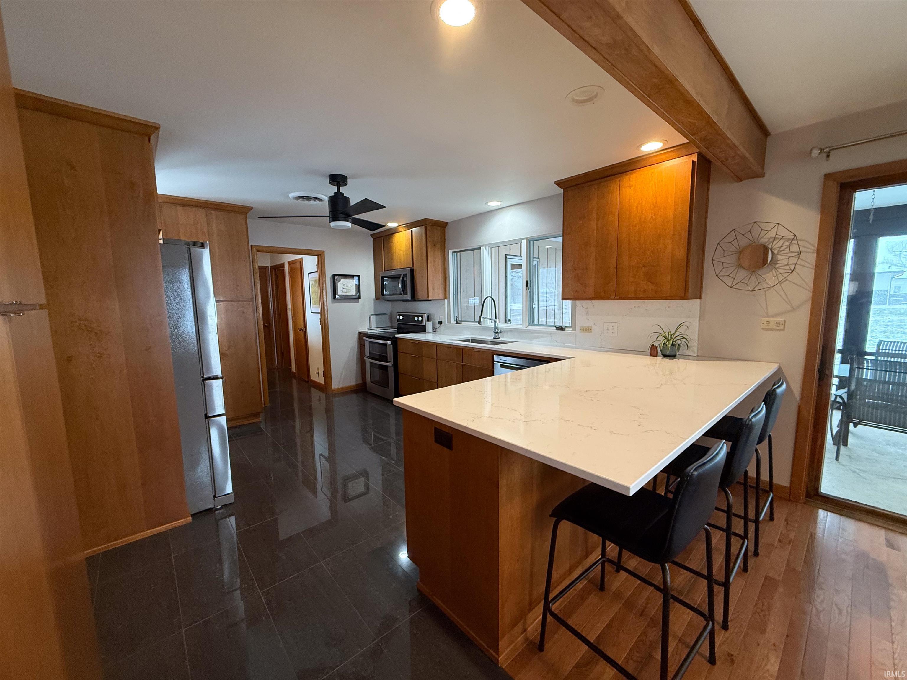 Kitchen featuring a peninsula, brown cabinets, stainless steel appliances, a ceiling fan, and a breakfast bar