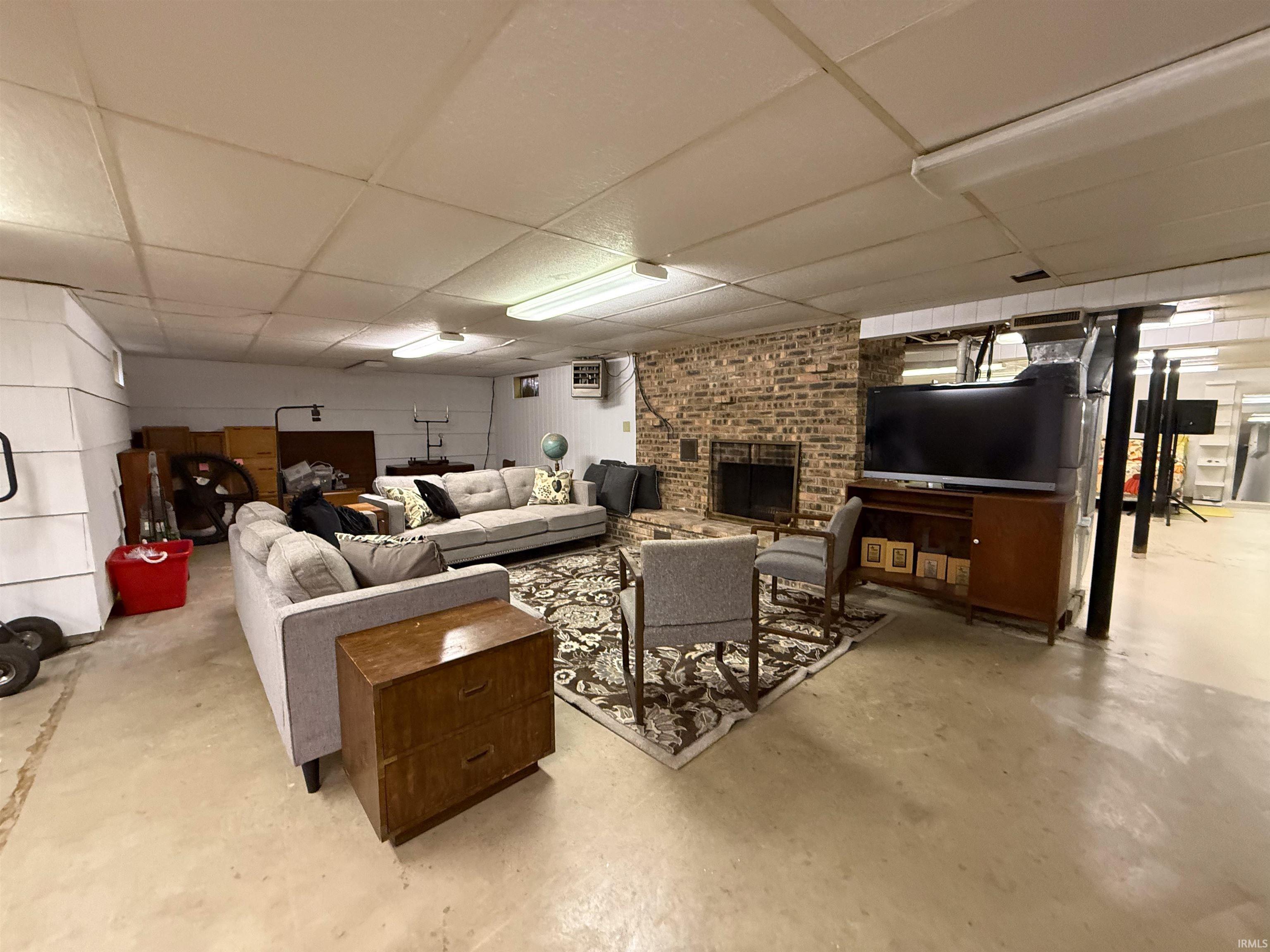 Living room featuring a drop ceiling, a brick fireplace, and concrete flooring