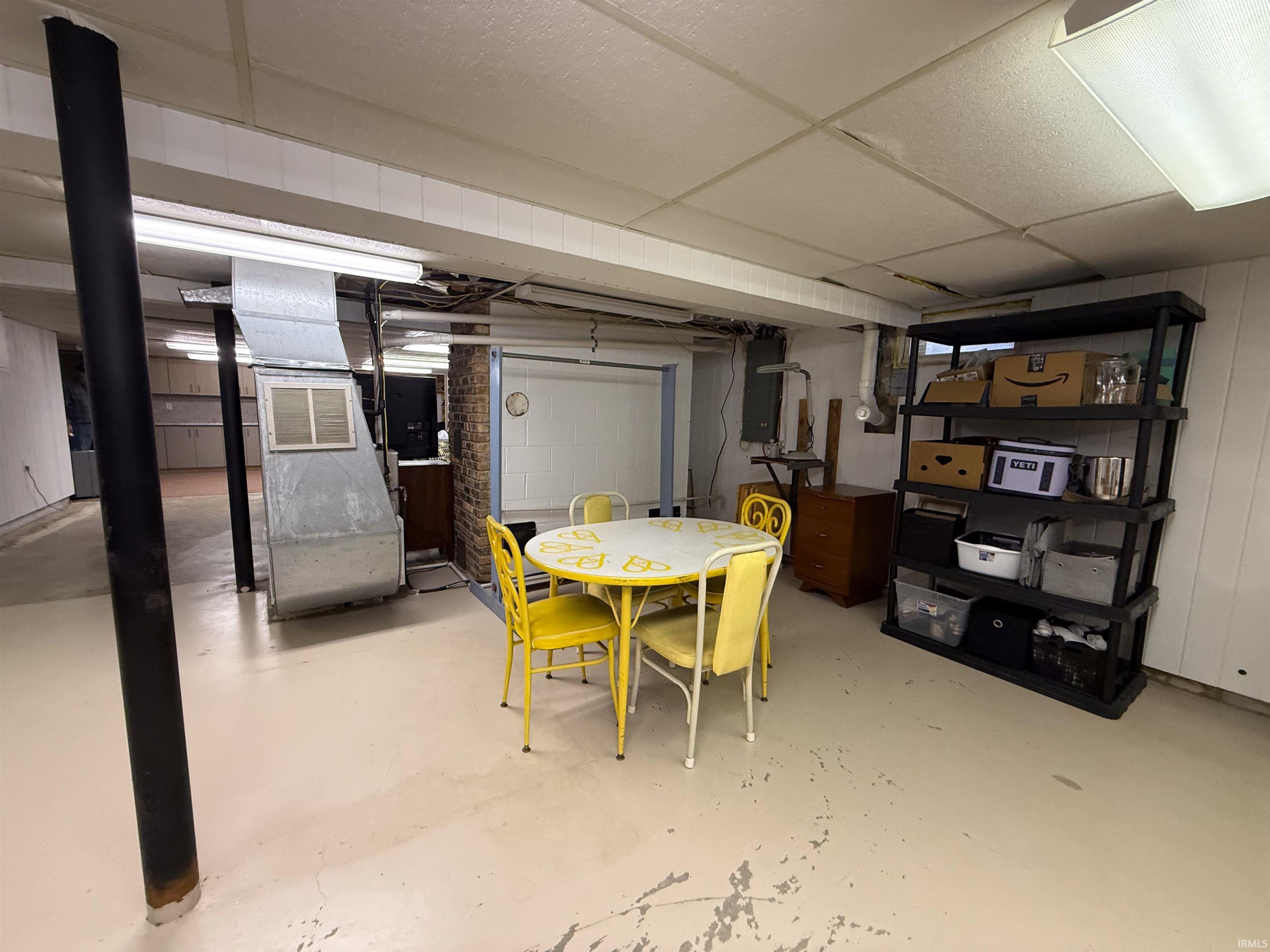 Basement featuring heating unit, a paneled ceiling, concrete block wall, and electric panel