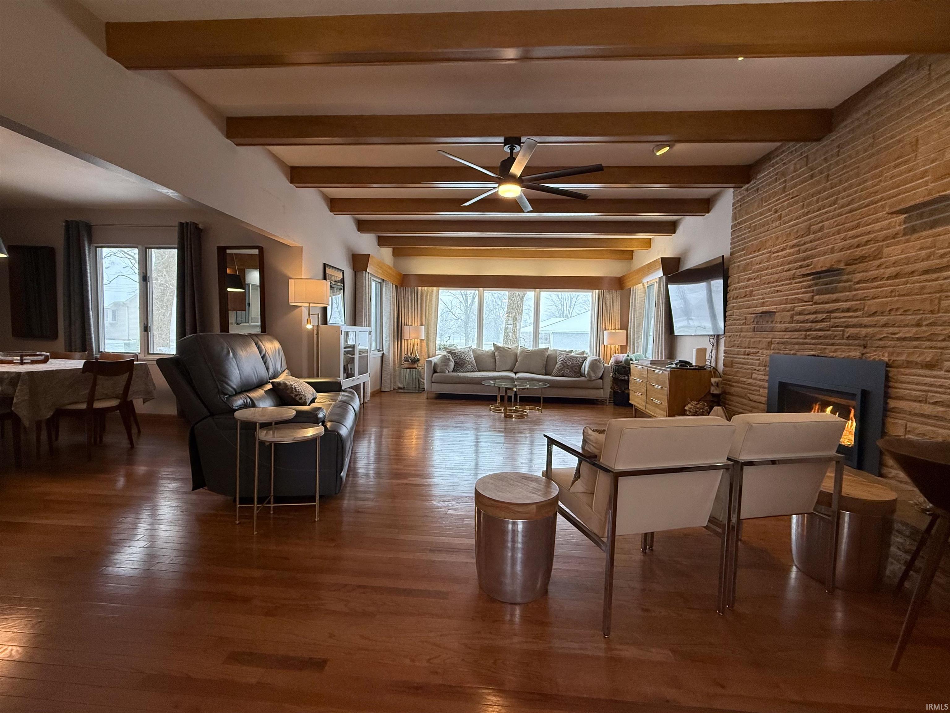 Living room featuring a large fireplace, beam ceiling, ceiling fan, and wood finished floors