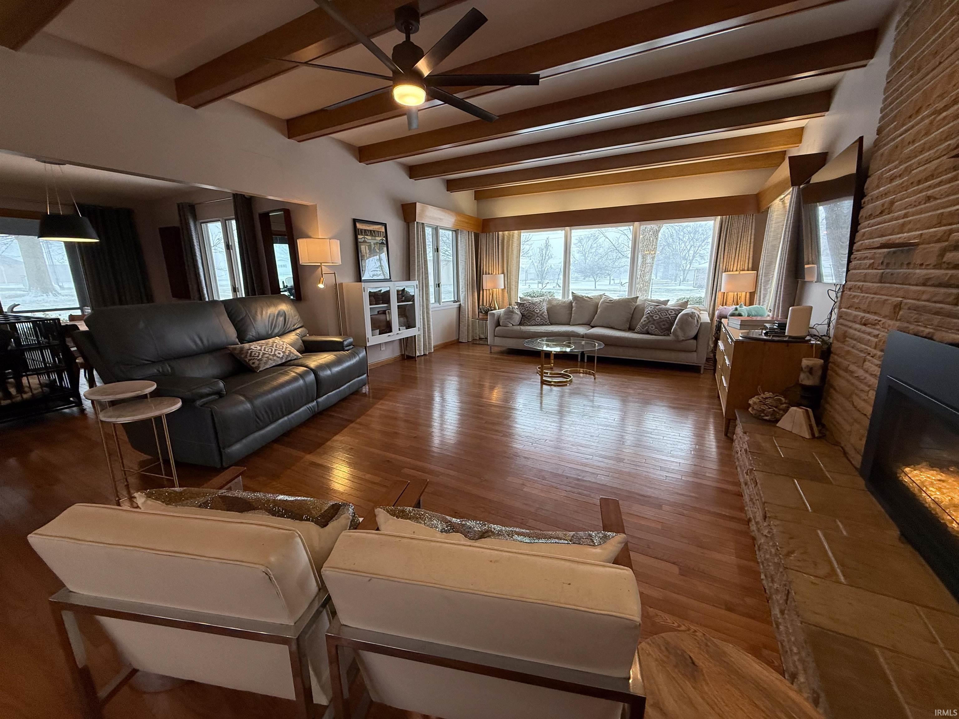 Living room featuring plenty of natural light, beam ceiling, a fireplace, ceiling fan, and hardwood / wood-style flooring