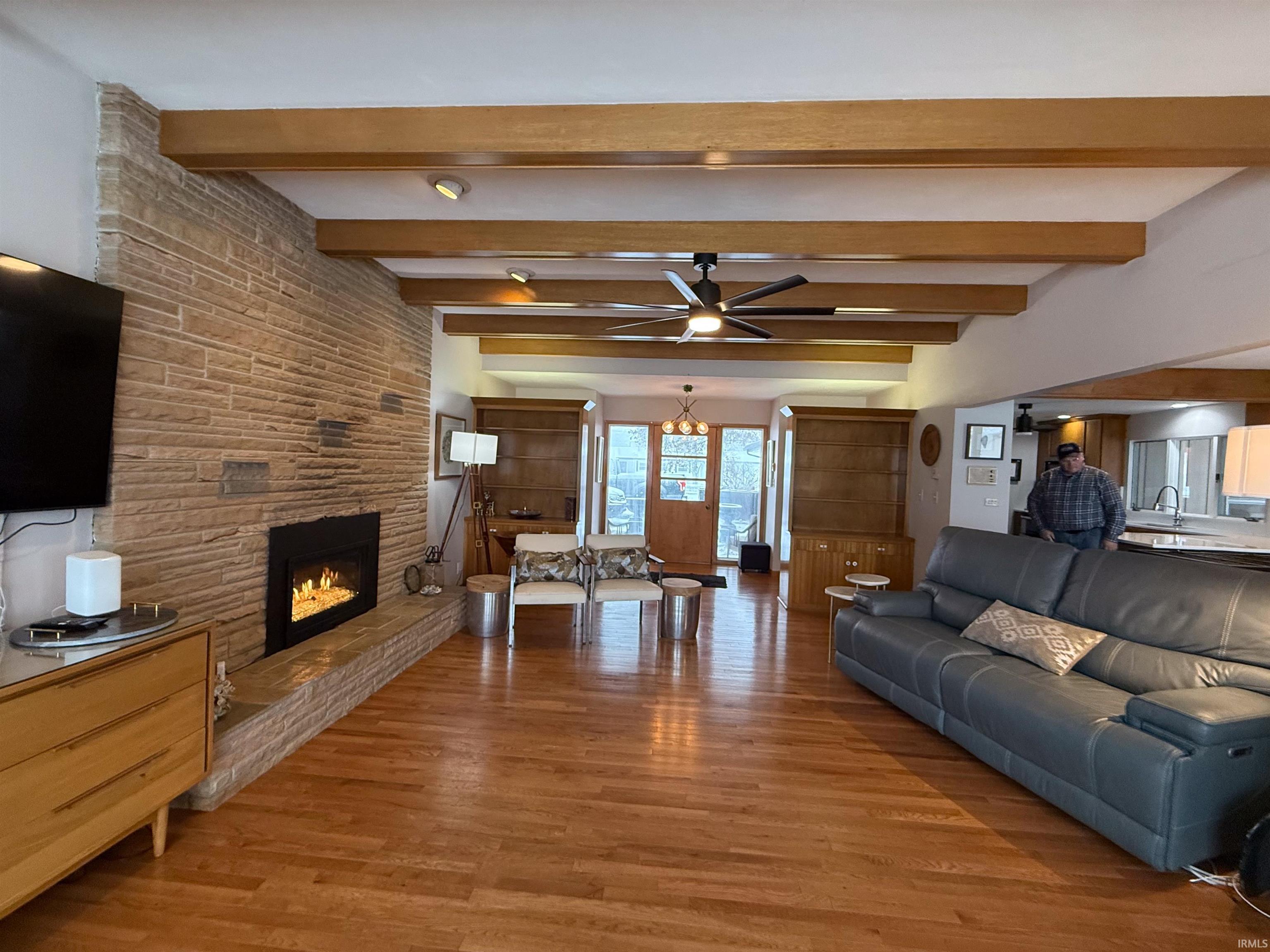Living area featuring light wood-style floors, a ceiling fan, a fireplace, and beamed ceiling
